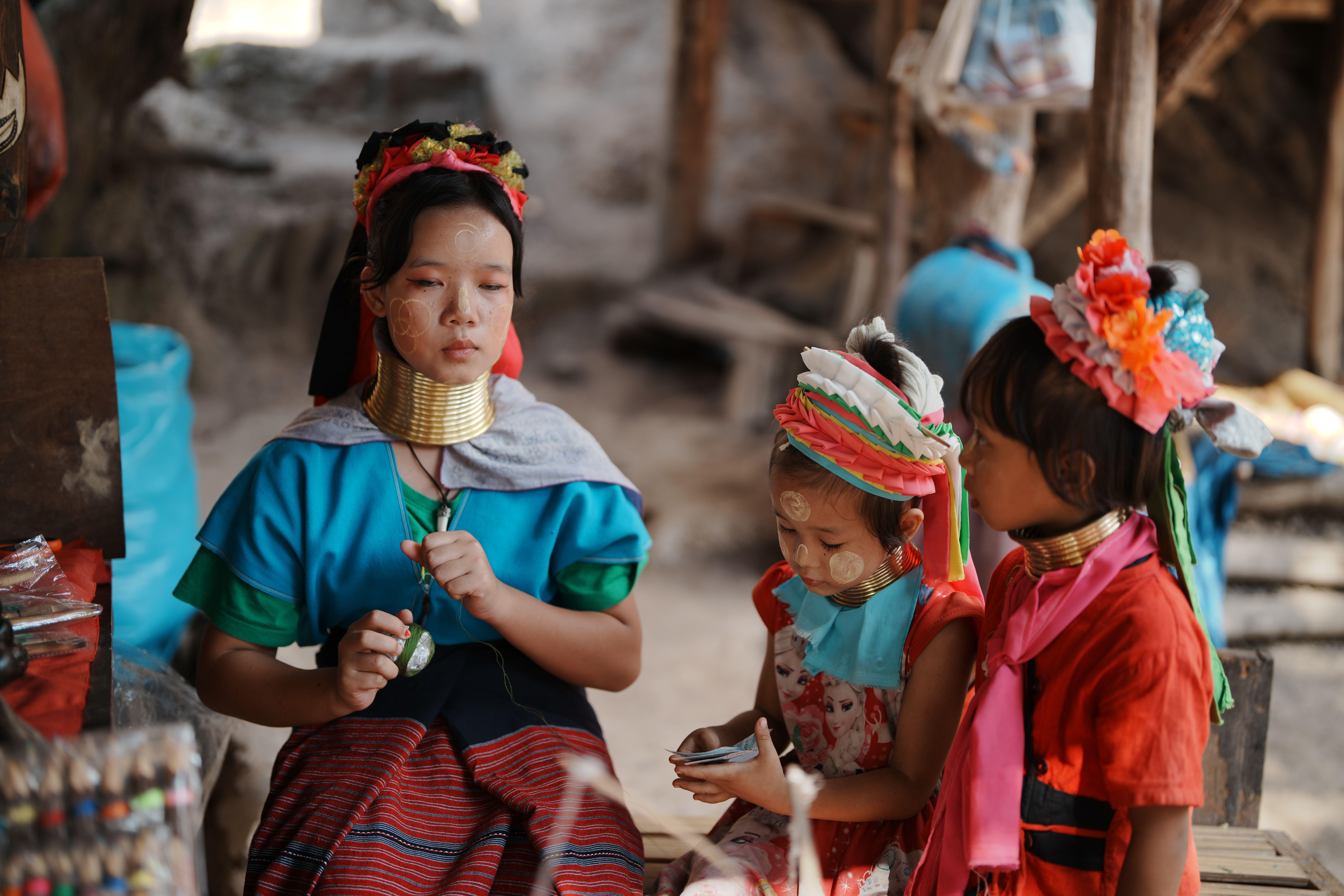 Young Long Neck Karen woman with children in traditional attire, outdoors.