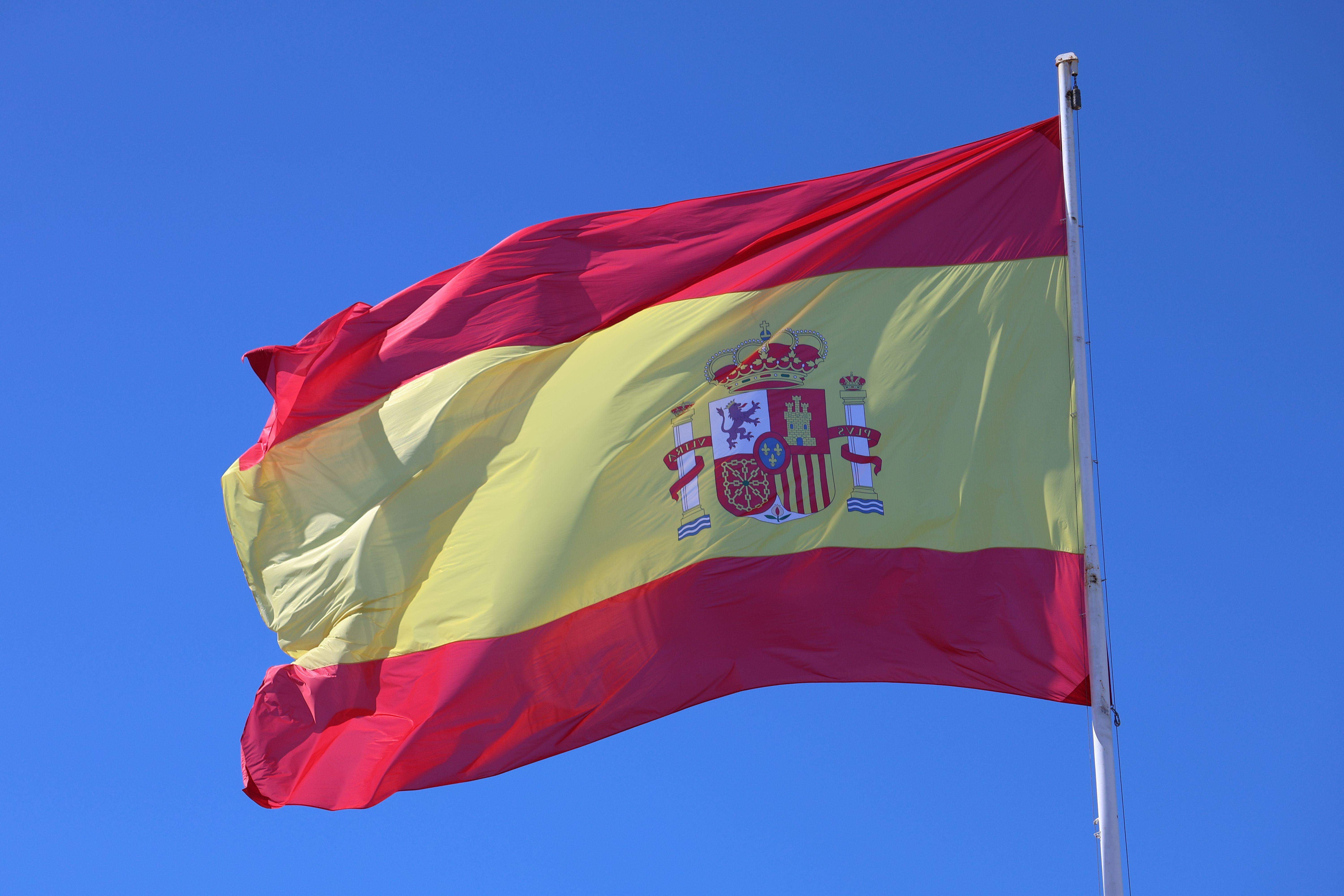Vibrant Spanish flag waving against a clear blue sky, emblematic of national pride.
