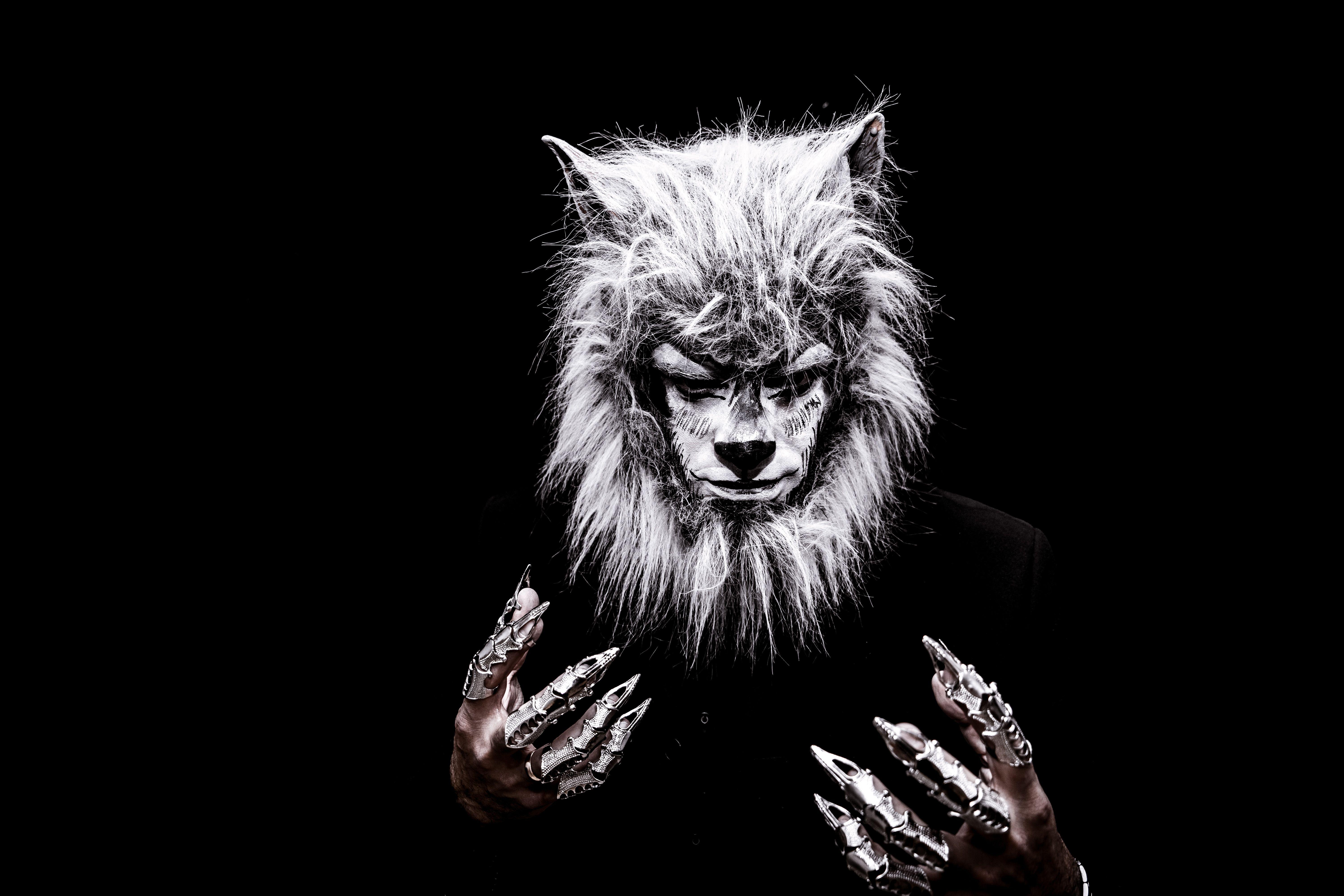 Striking portrait of an adult in a realistic werewolf costume with metallic claws against a black background.