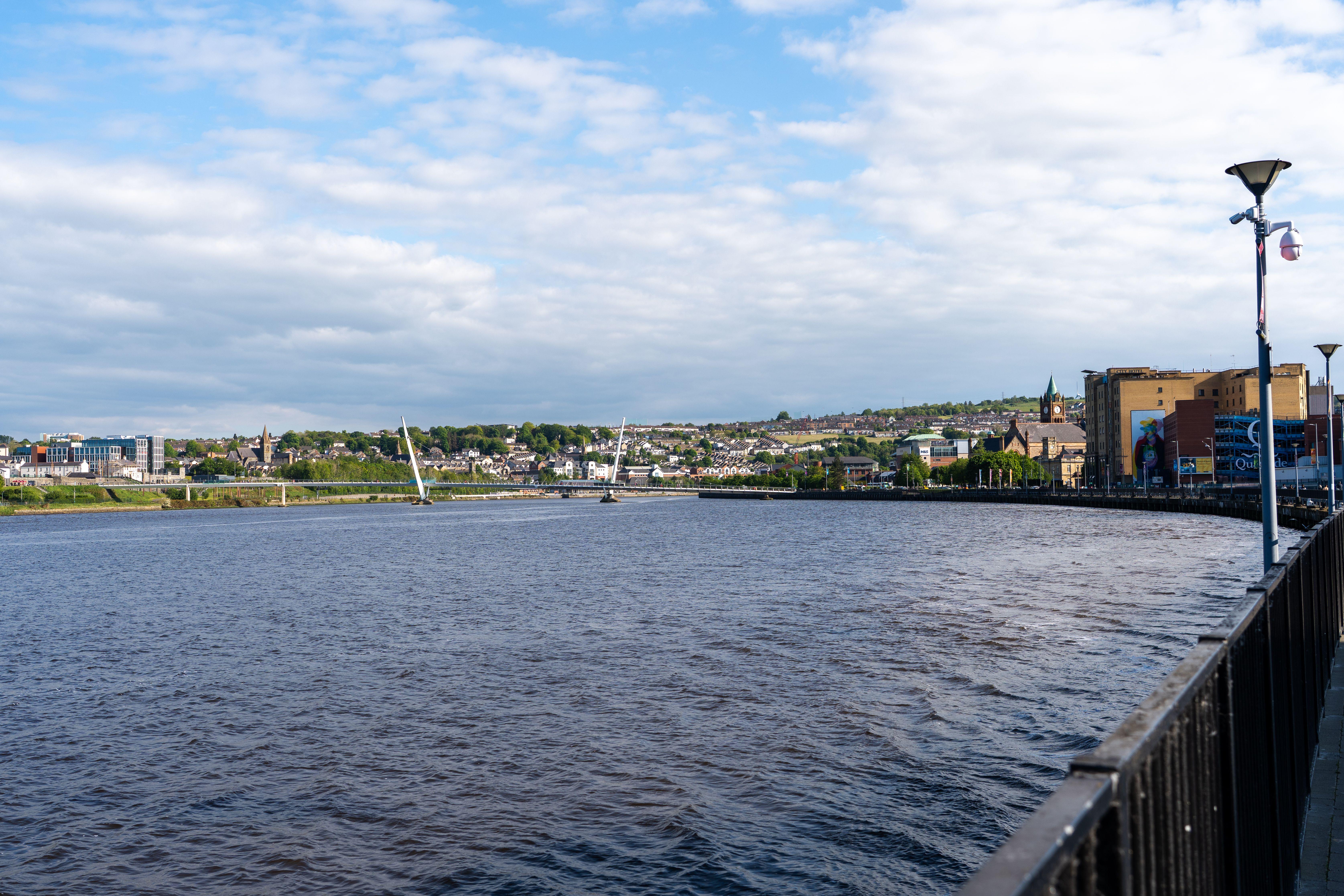 Scenic view of the Peace Bridge spanning the River Foyle in Derry, Ireland under clear blue skies.