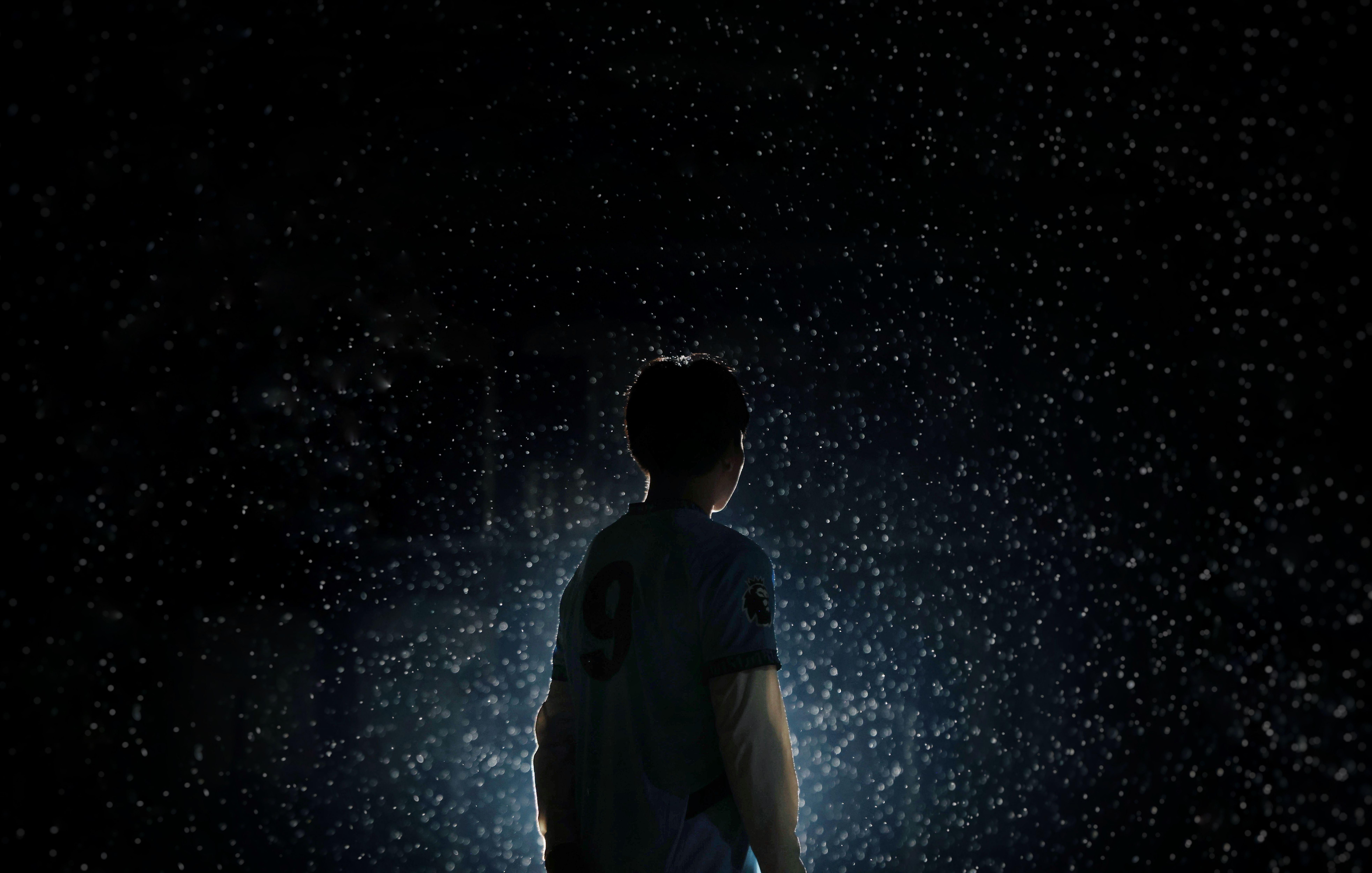 A dramatic silhouette of a soccer player standing in rain with backlit lighting.