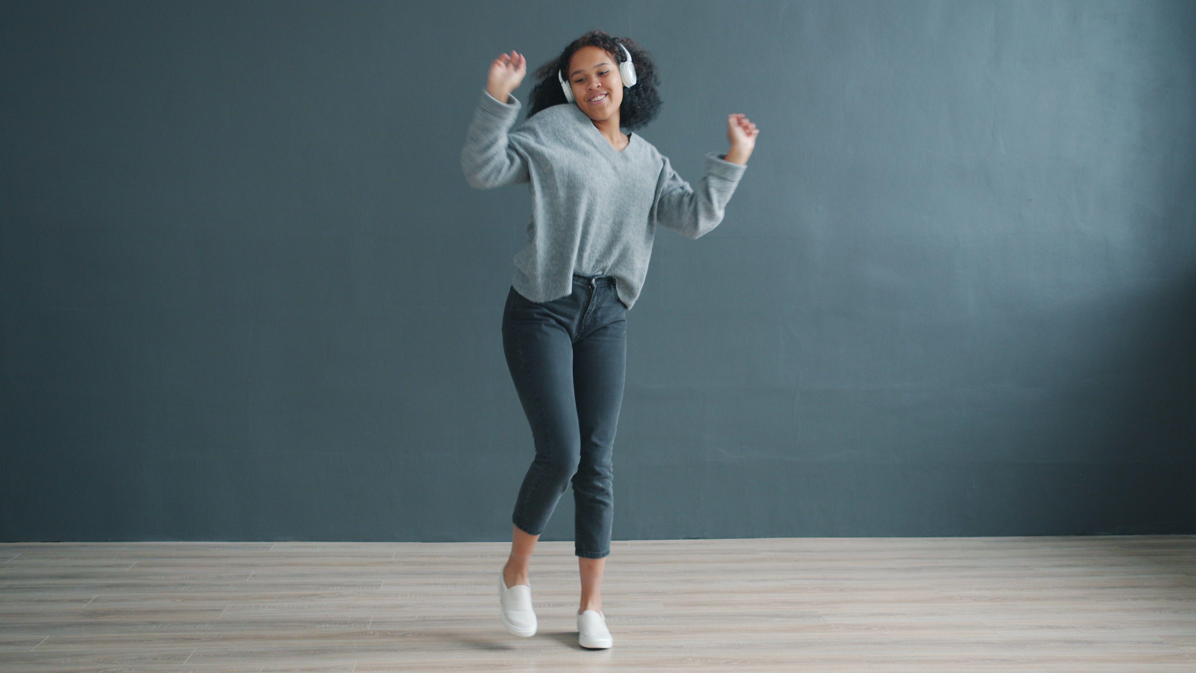 Happy young woman dancing with headphones on, enjoying music in a modern room.
