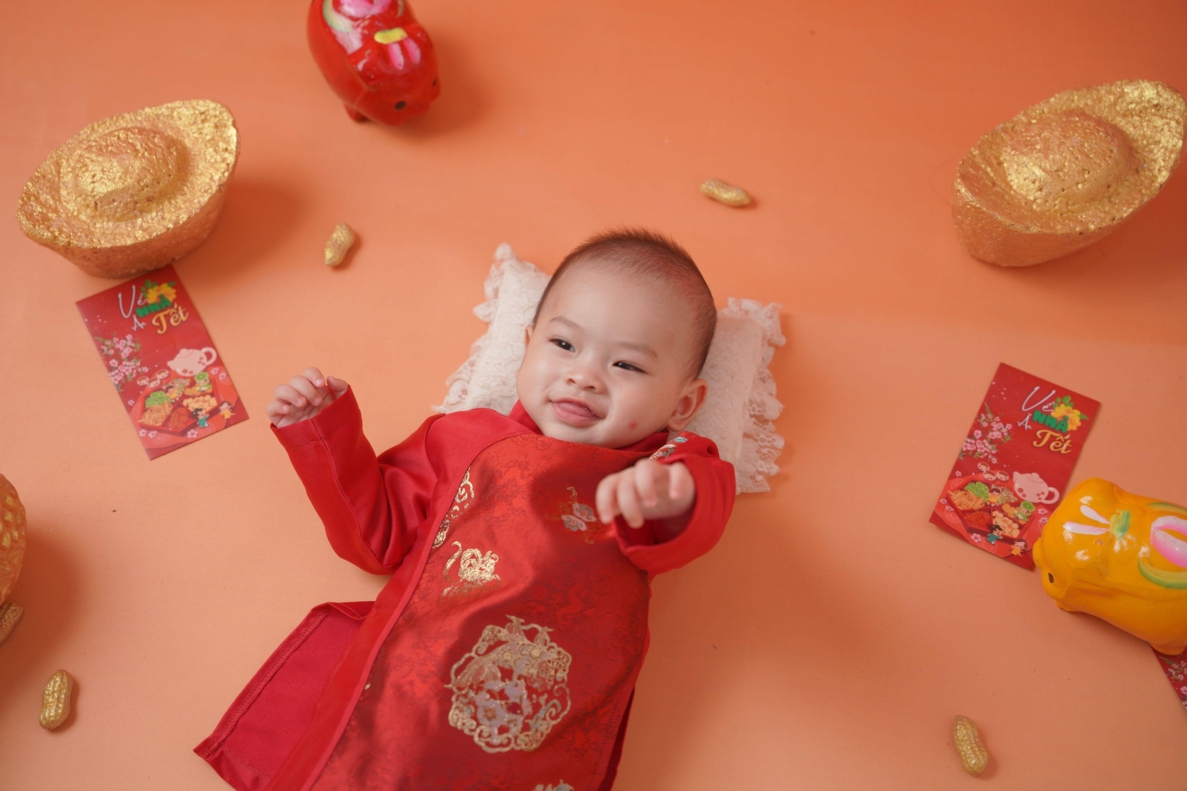 Smiling baby dressed in traditional attire for Lunar New Year surrounded by festive decorations.