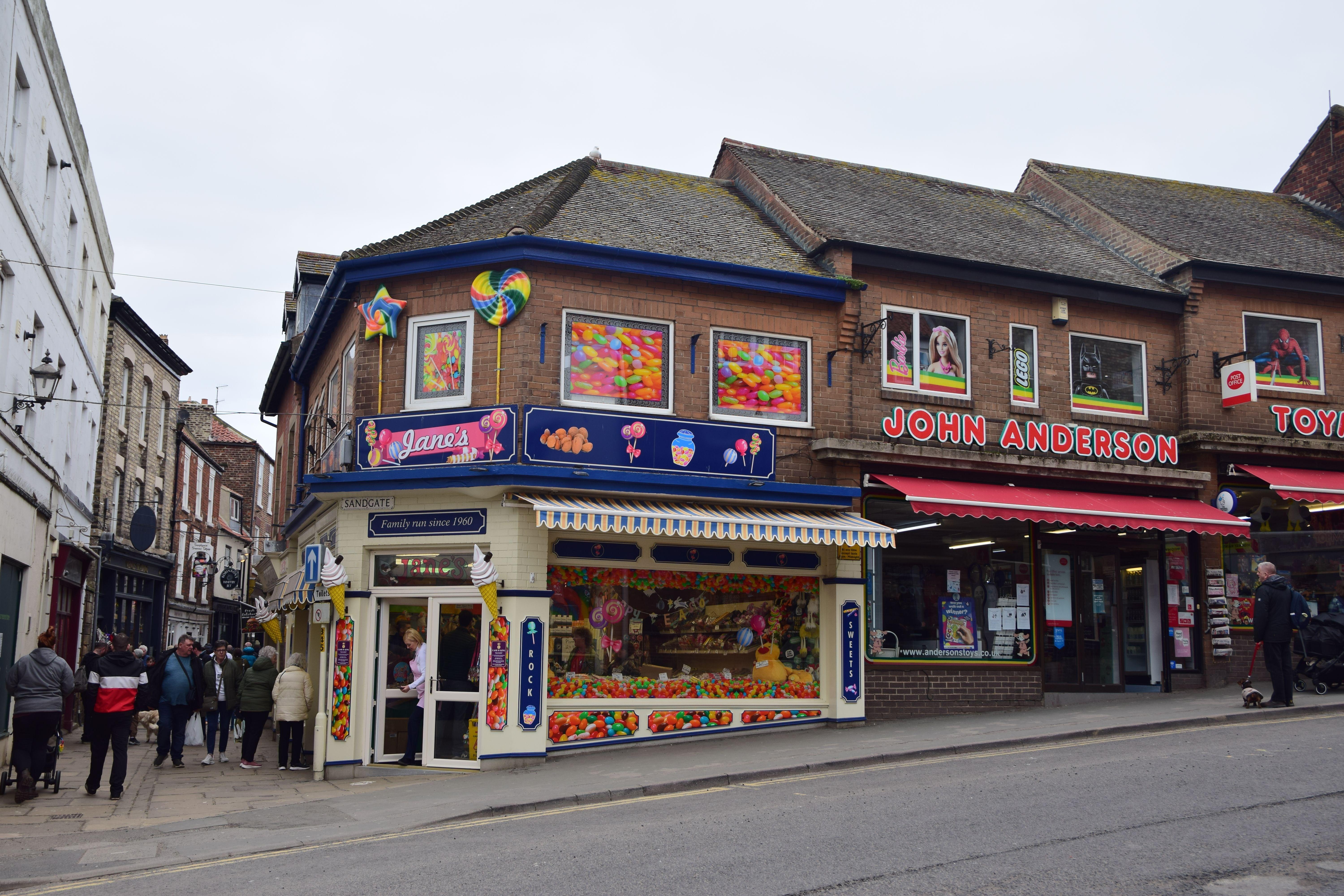 Vibrant candy shop and toy store on a bustling street corner with pedestrians.