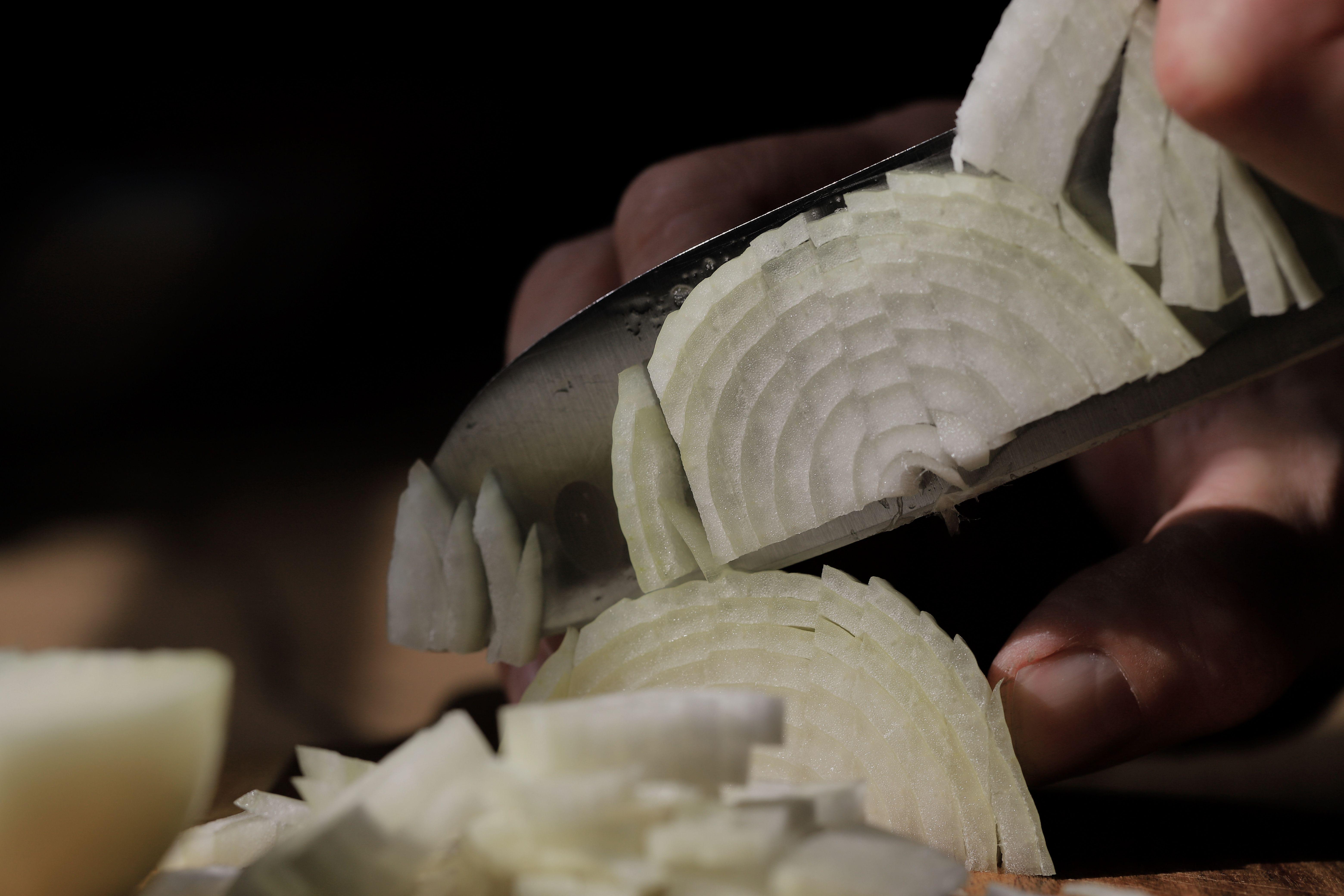 Detailed shot of slicing white onions with a sharp knife, perfect for cooking themes.