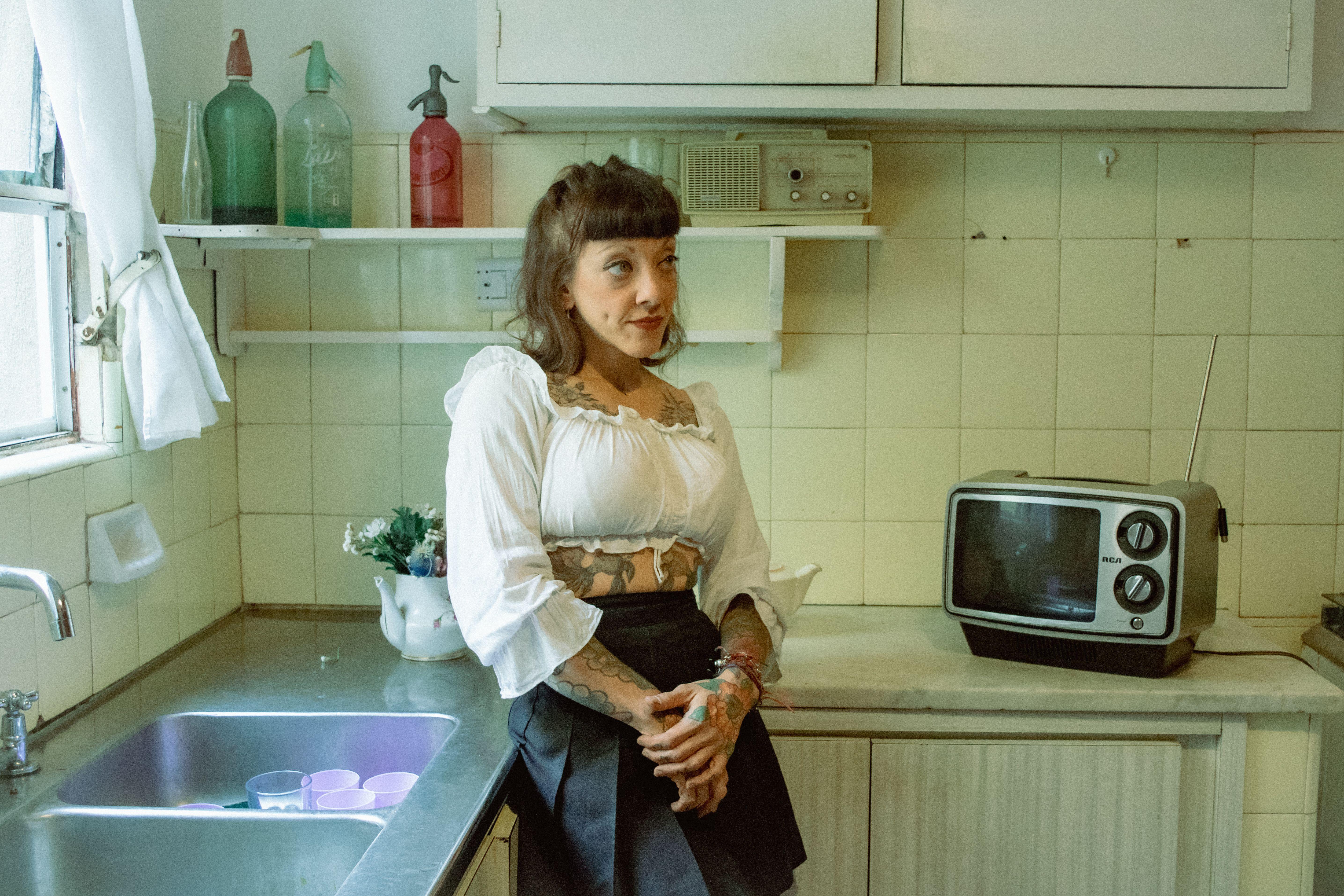 Tattooed woman in a vintage kitchen with retro decor and appliances, exuding a classic vibe.