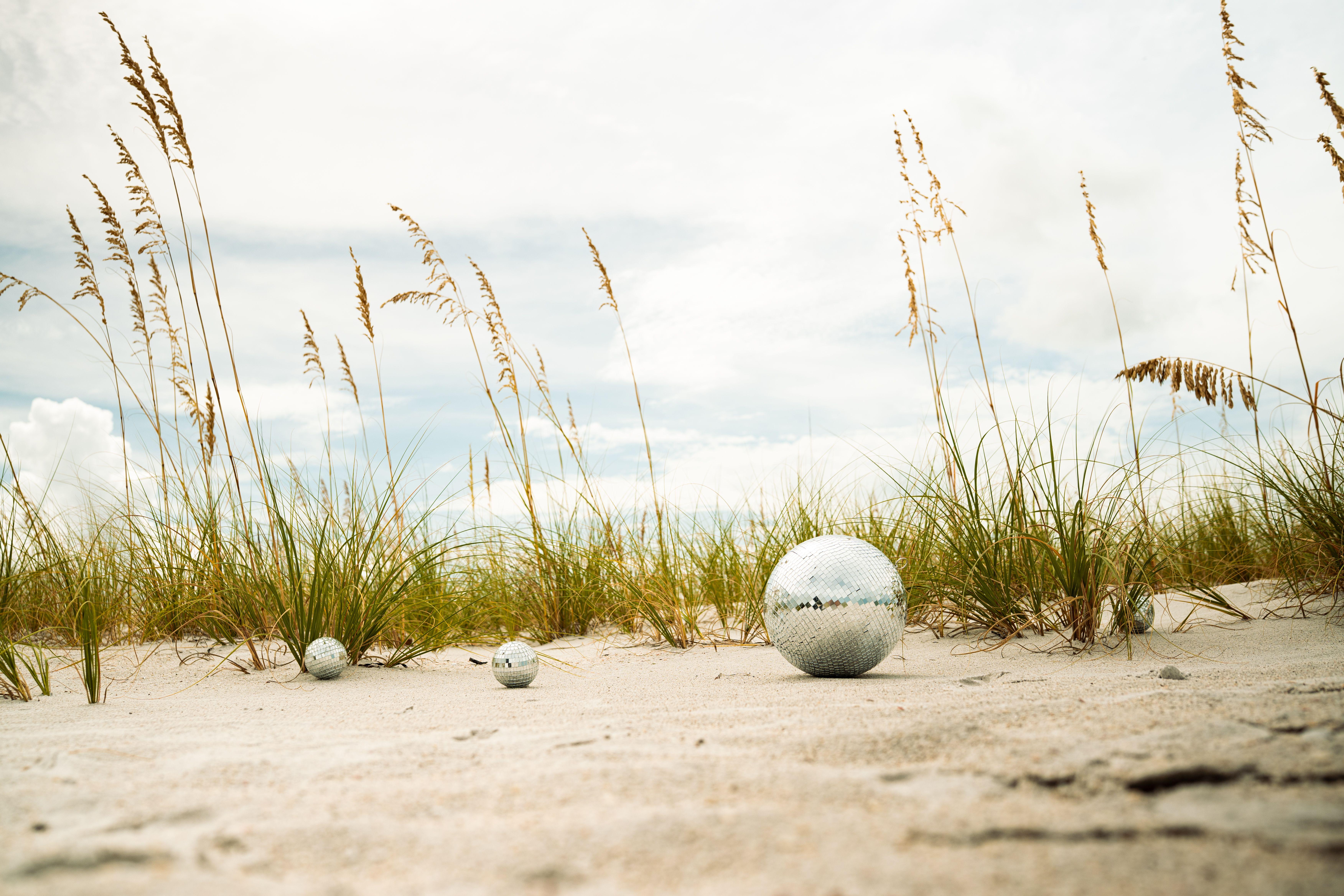 Serene beach with ornamental reflective spheres and tall grass under a cloudy sky.