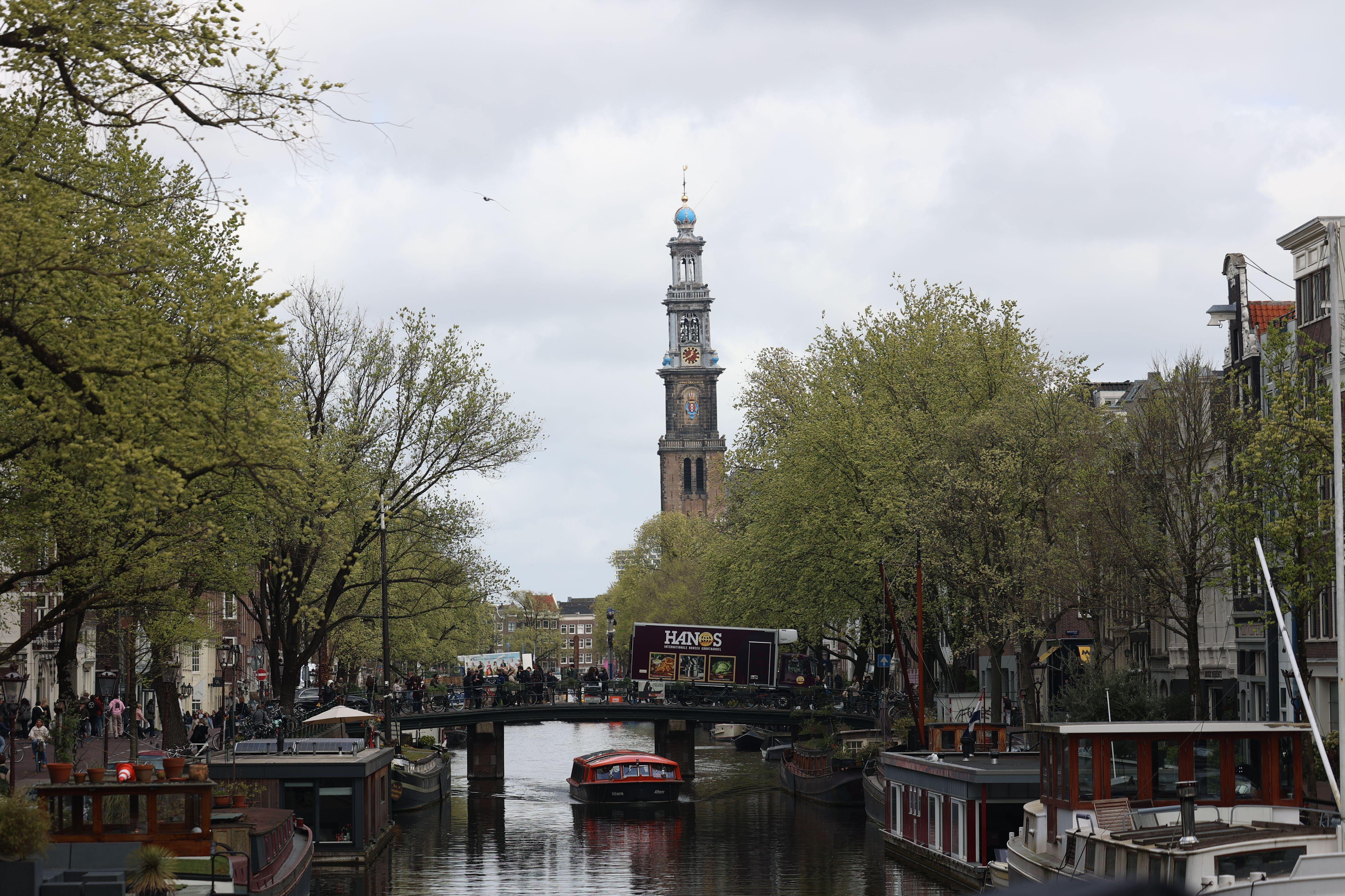 Scenic view of Amsterdam's Westerkerk tower and canal with boats and greenery in spring.