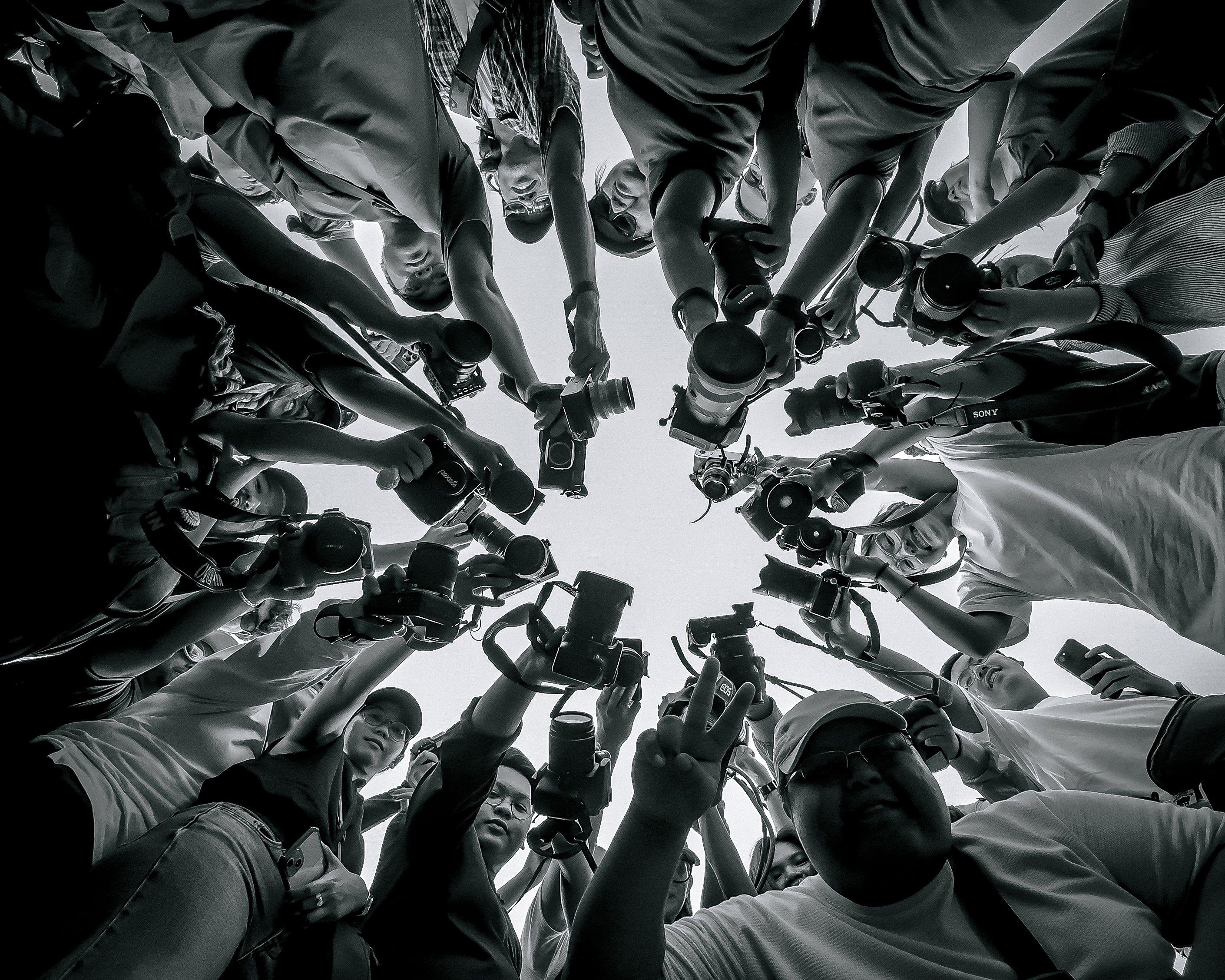 A diverse group of photographers pointing cameras, captured from below, creating a powerful visual impact.