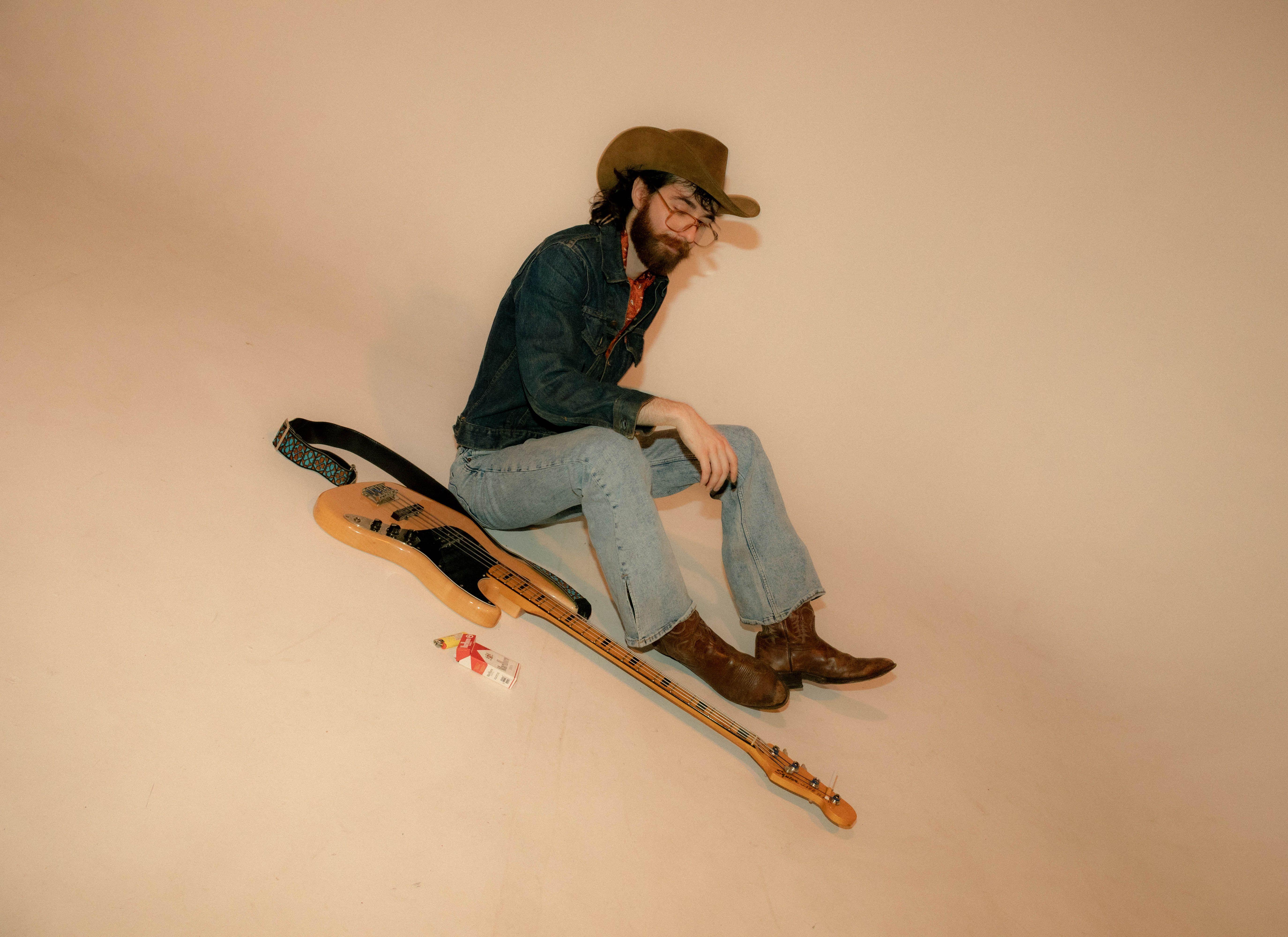 Young male musician in cowboy hat and denim posing with electric guitar in a studio setting.
