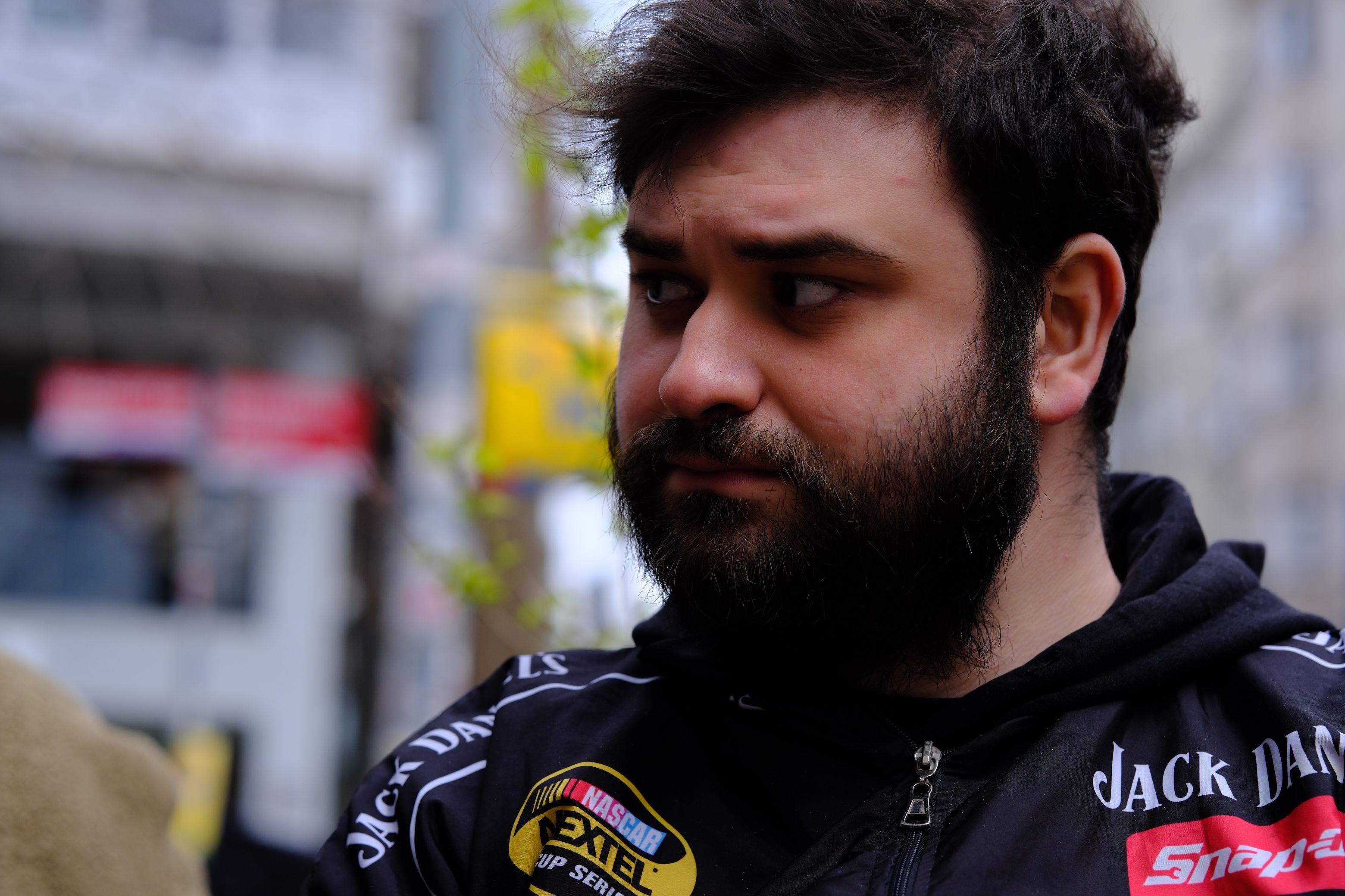 A thoughtful man looking aside in an urban setting, wearing a branded black jacket.