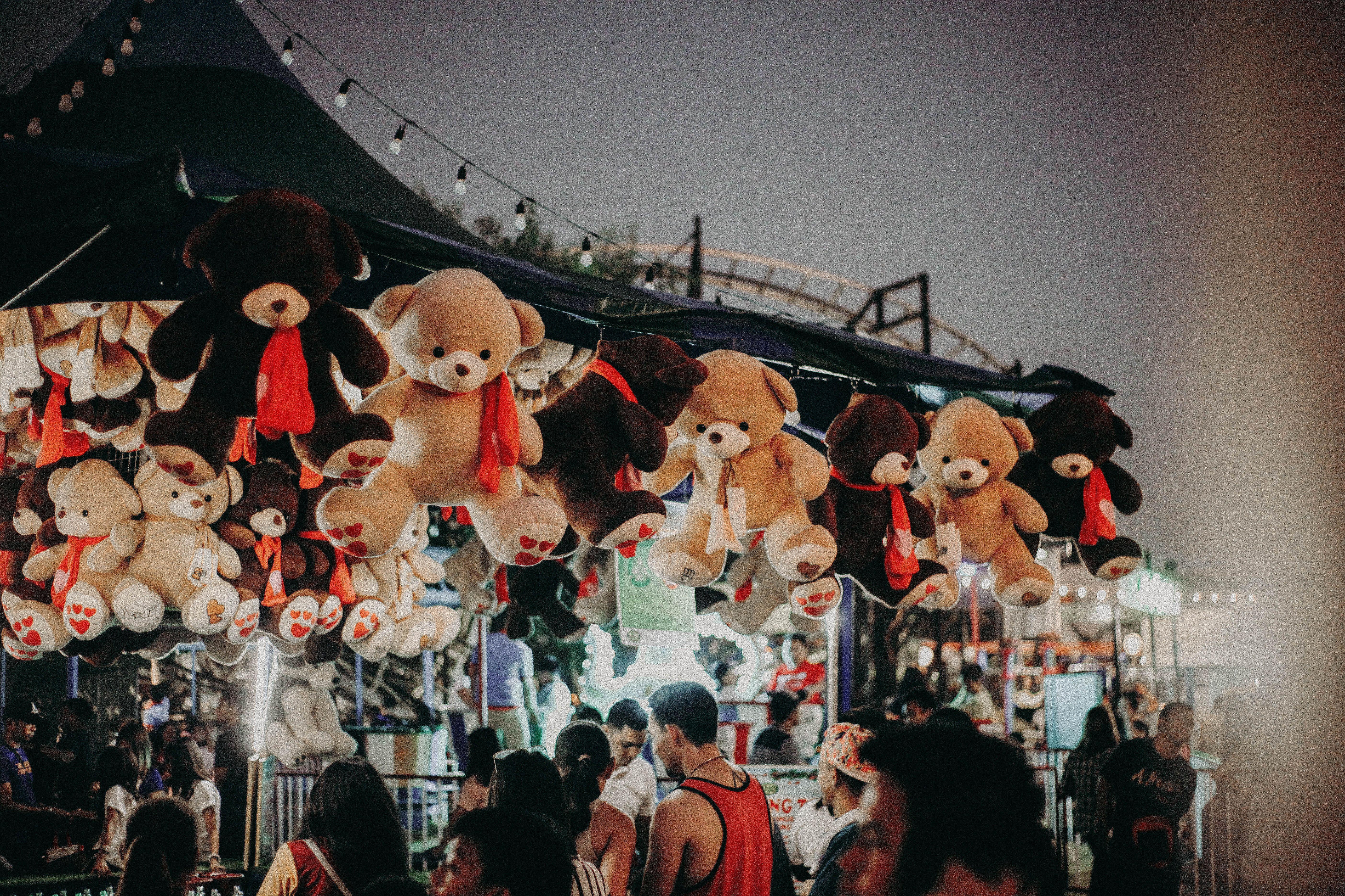 A bustling carnival scene at night featuring teddy bear prizes and a lively crowd.