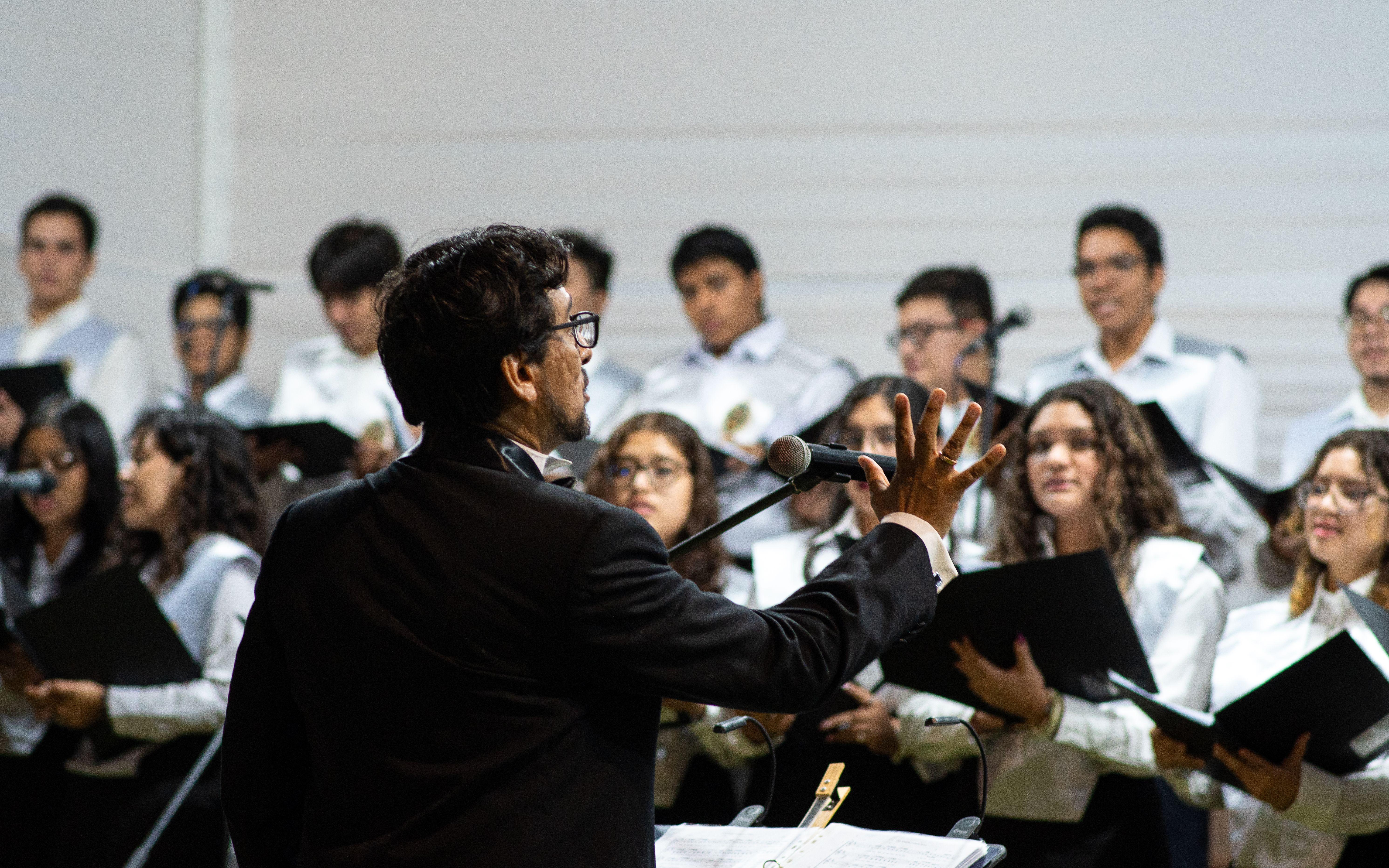 A university choir performing indoors under the direction of a conductor during a ceremony in Piura, Peru.