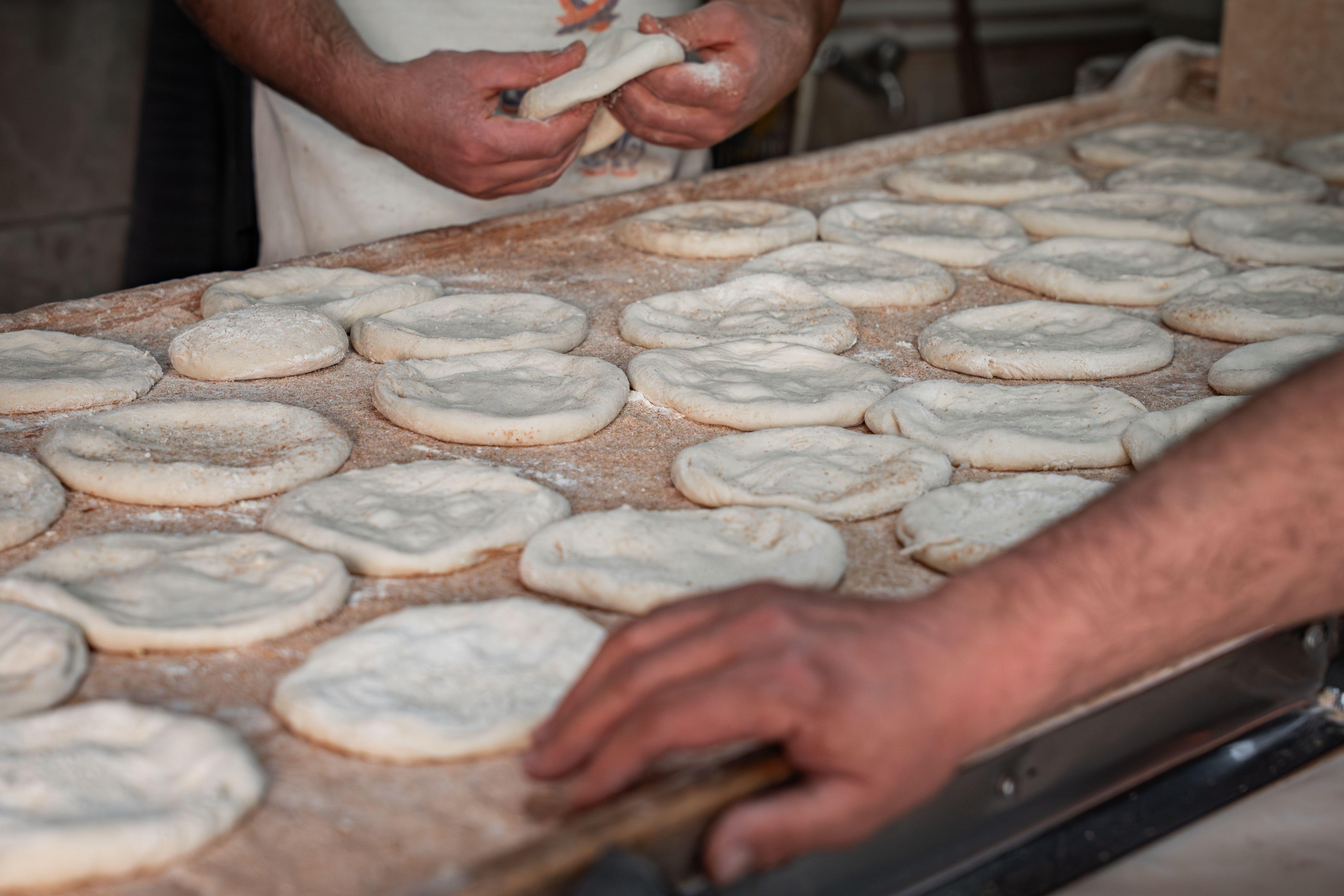Artisan bakers shaping fresh pita bread dough by hand in a traditional bakery setting.
