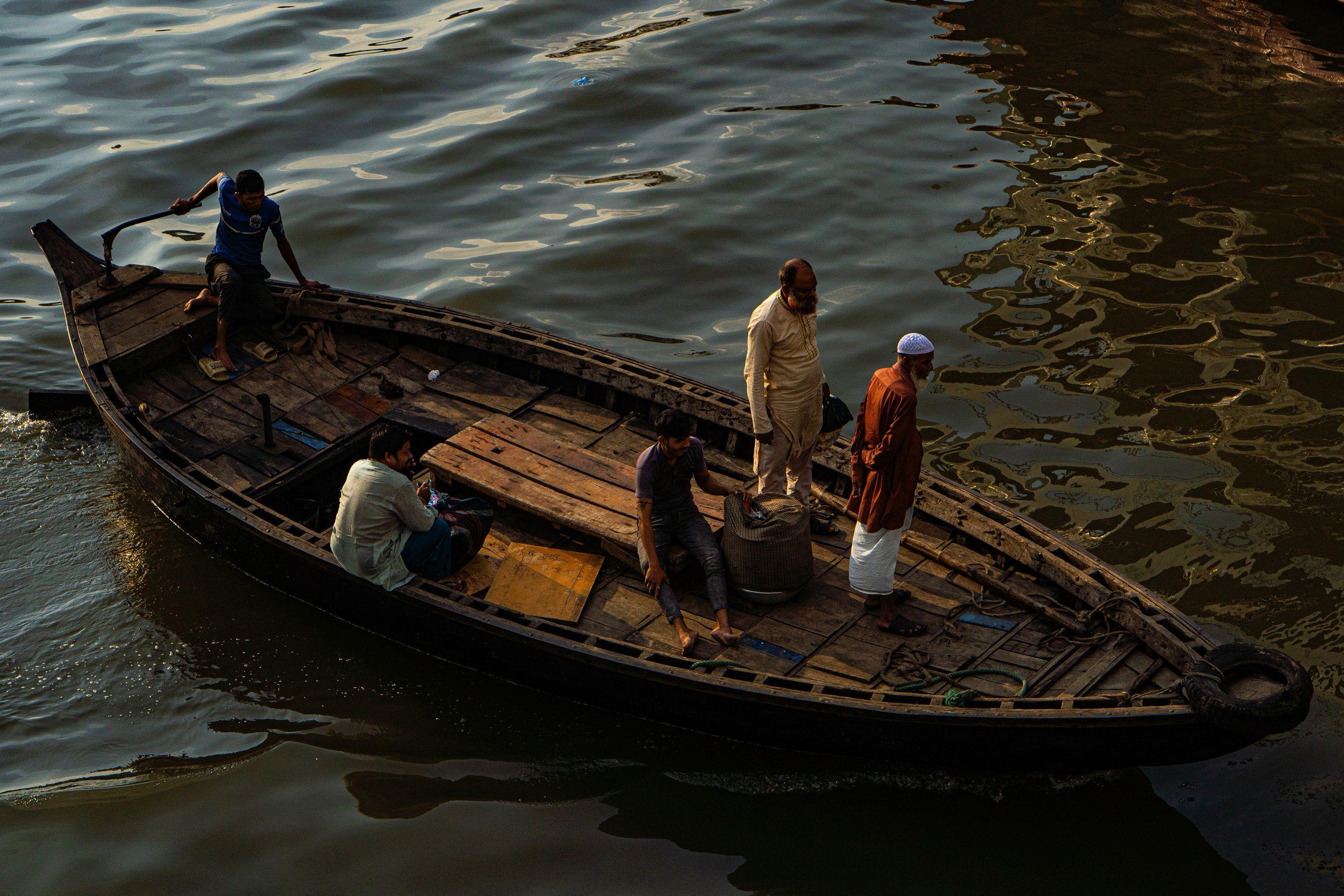 A group of people traveling on a wooden boat in Dhaka's Buriganga River, depicting local transportation.