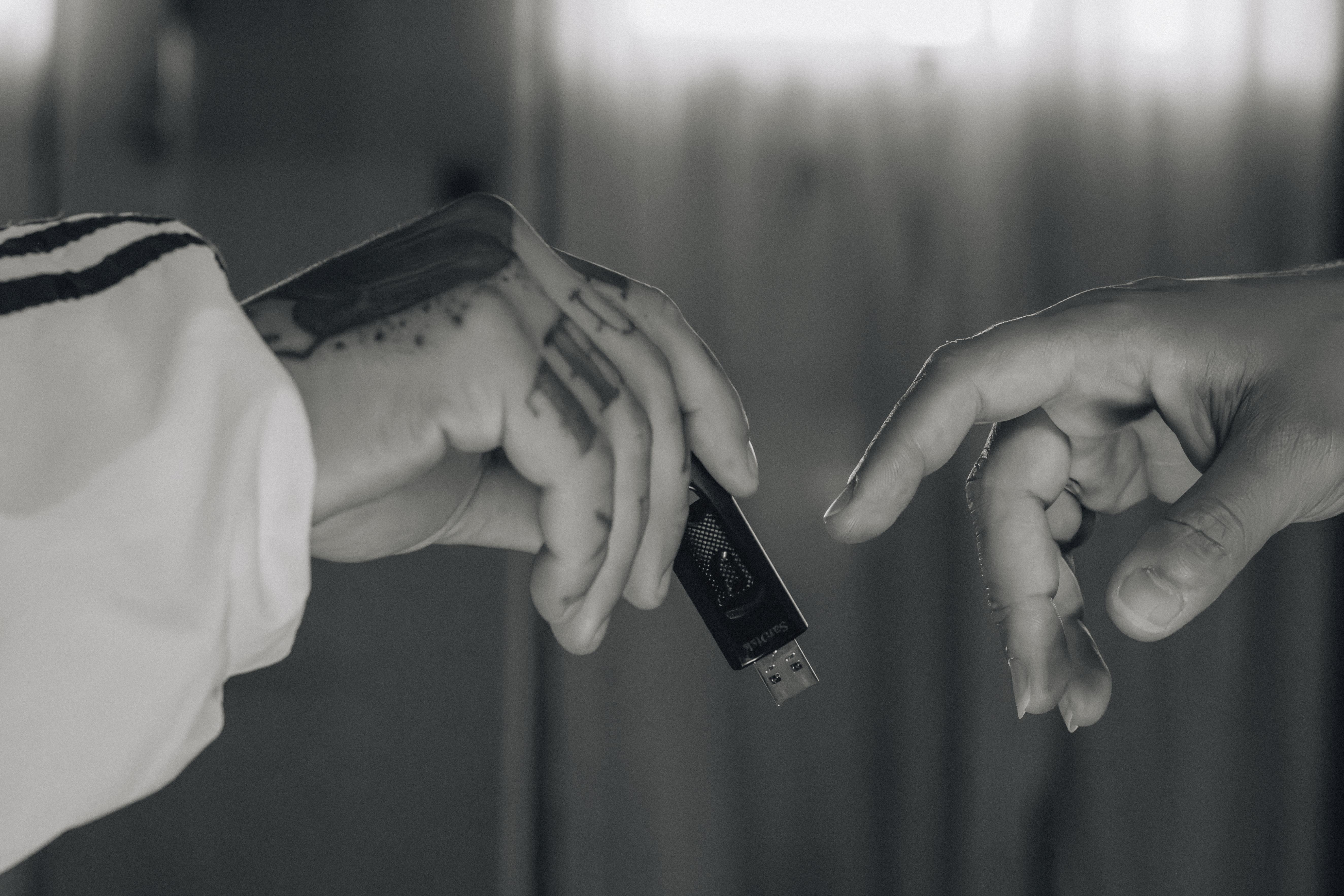 Close up view of two hands exchanging a USB drive against a blurred background.