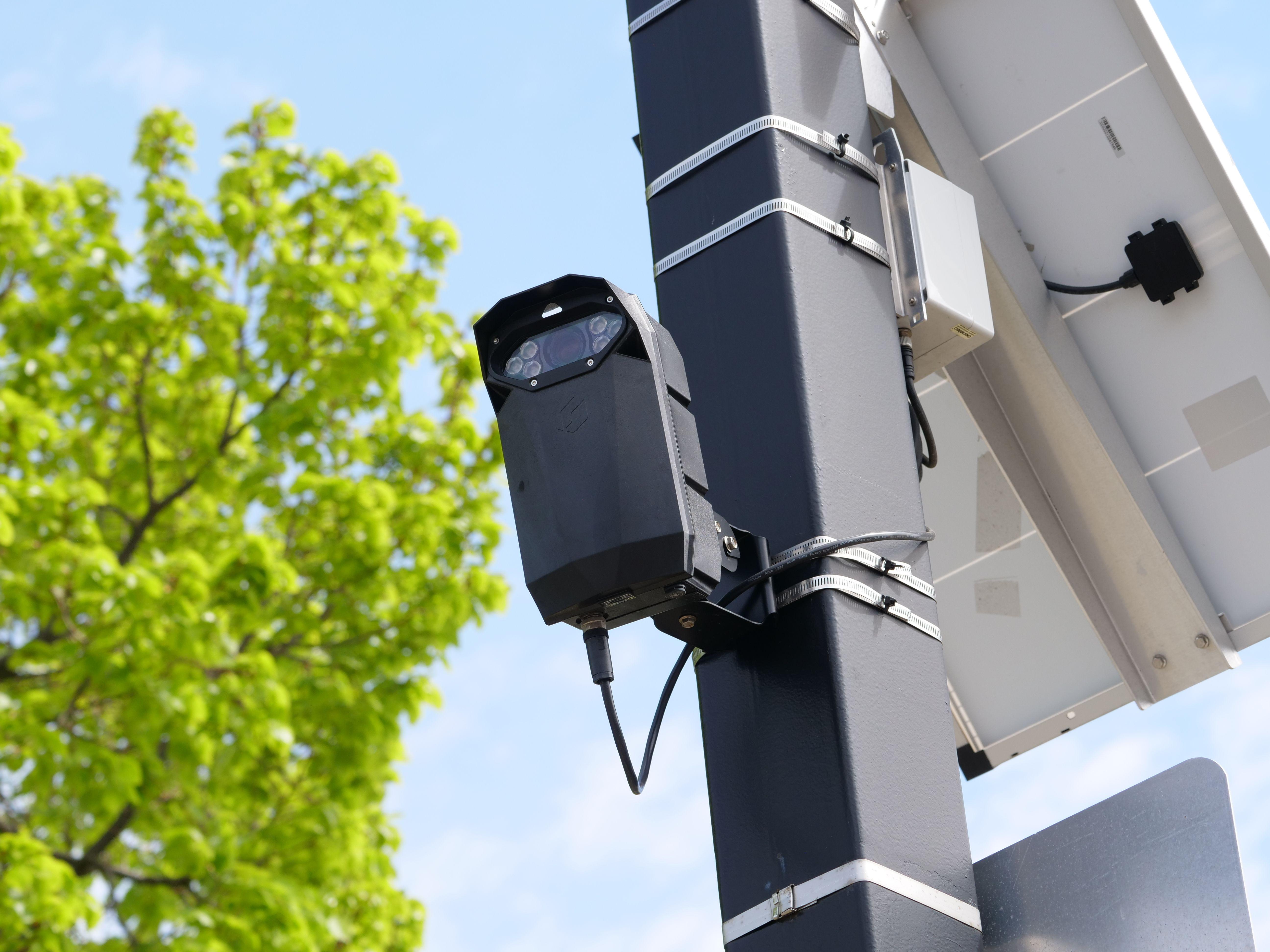 A modern surveillance camera powered by solar energy mounted on a street pole.