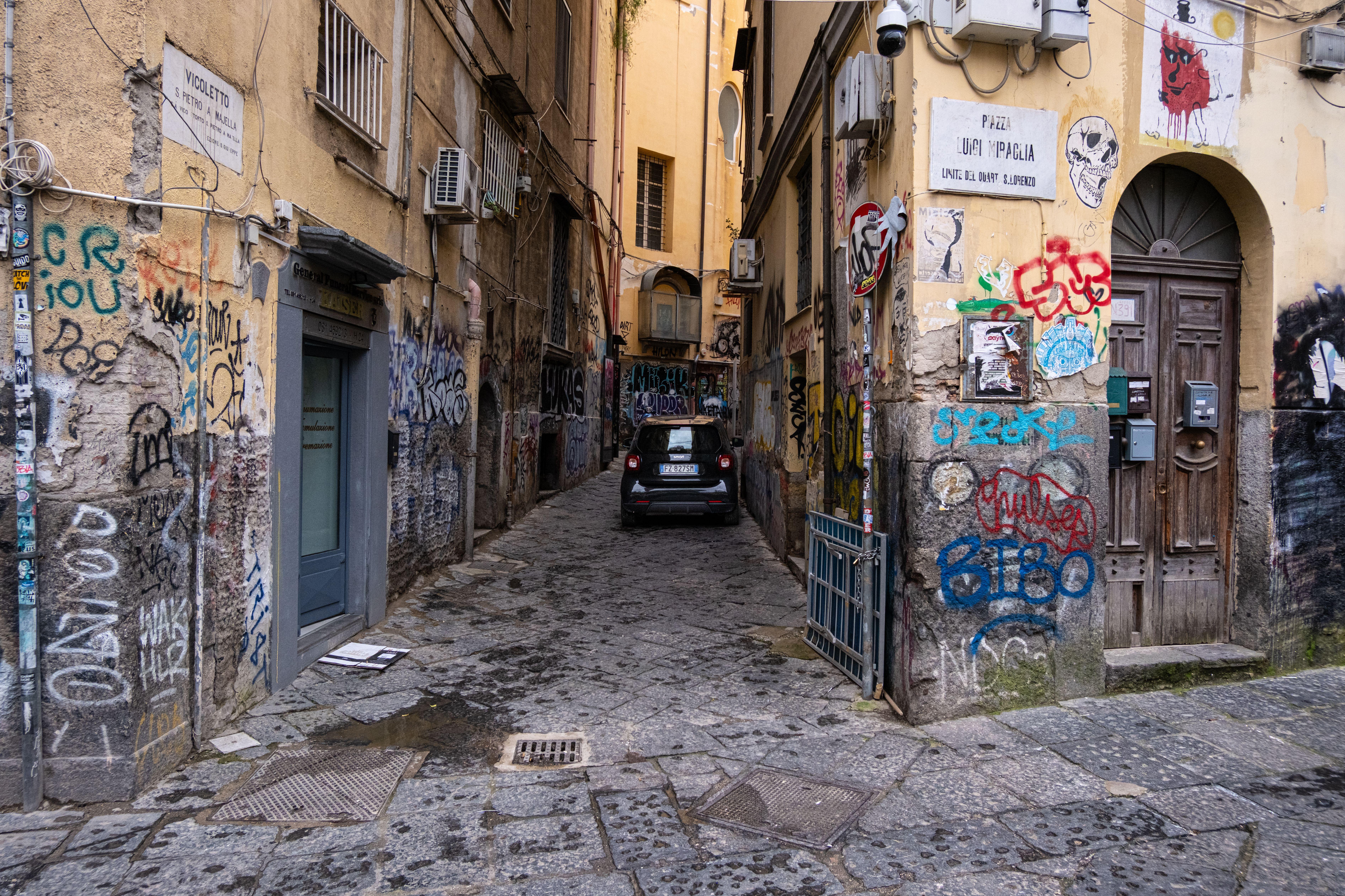 A narrow alley in Naples with colorful graffiti and an old building facade.
