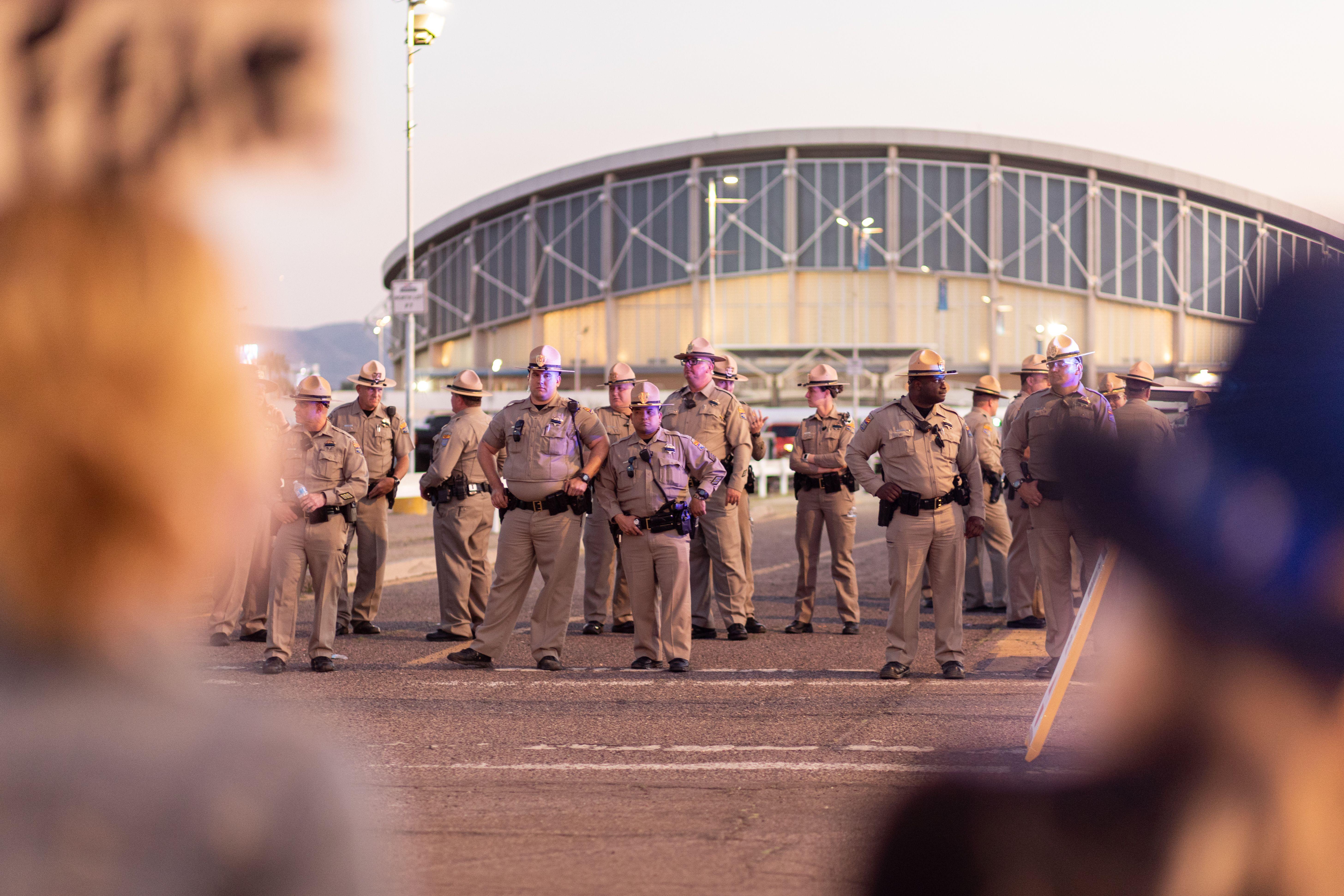A row of police officers in uniform standing outside a large building during a public event in Arizona.