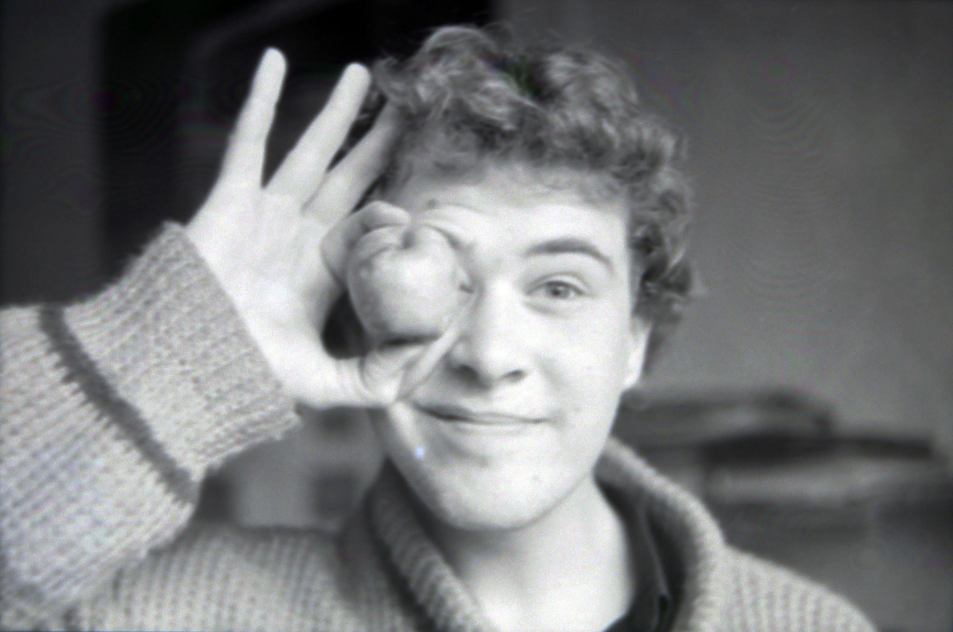 A black and white portrait of a young man playfully holding an object to his eye.