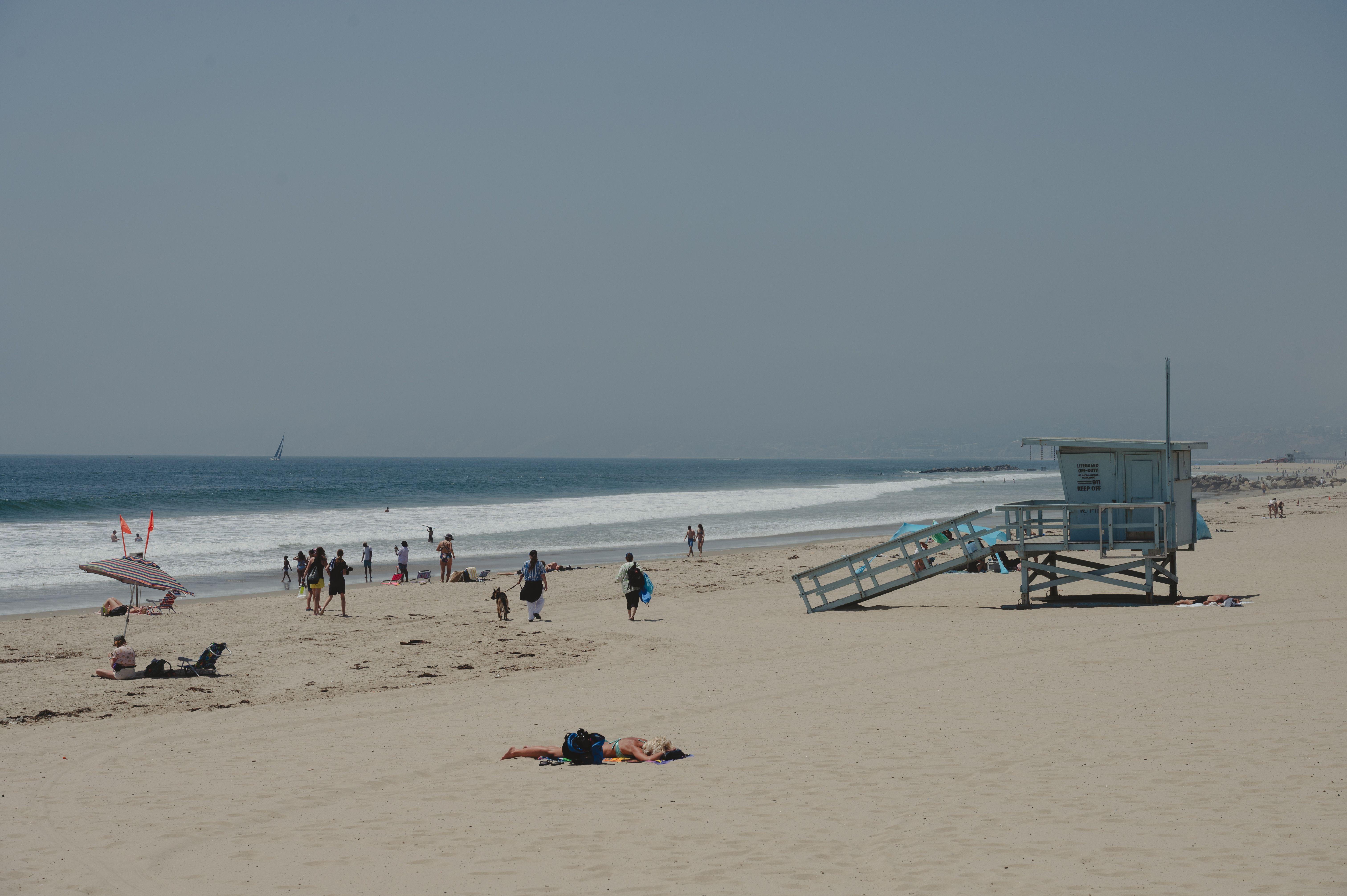 Sunbathers and beachgoers at Santa Monica Beach with iconic lifeguard tower on a sunny summer day.