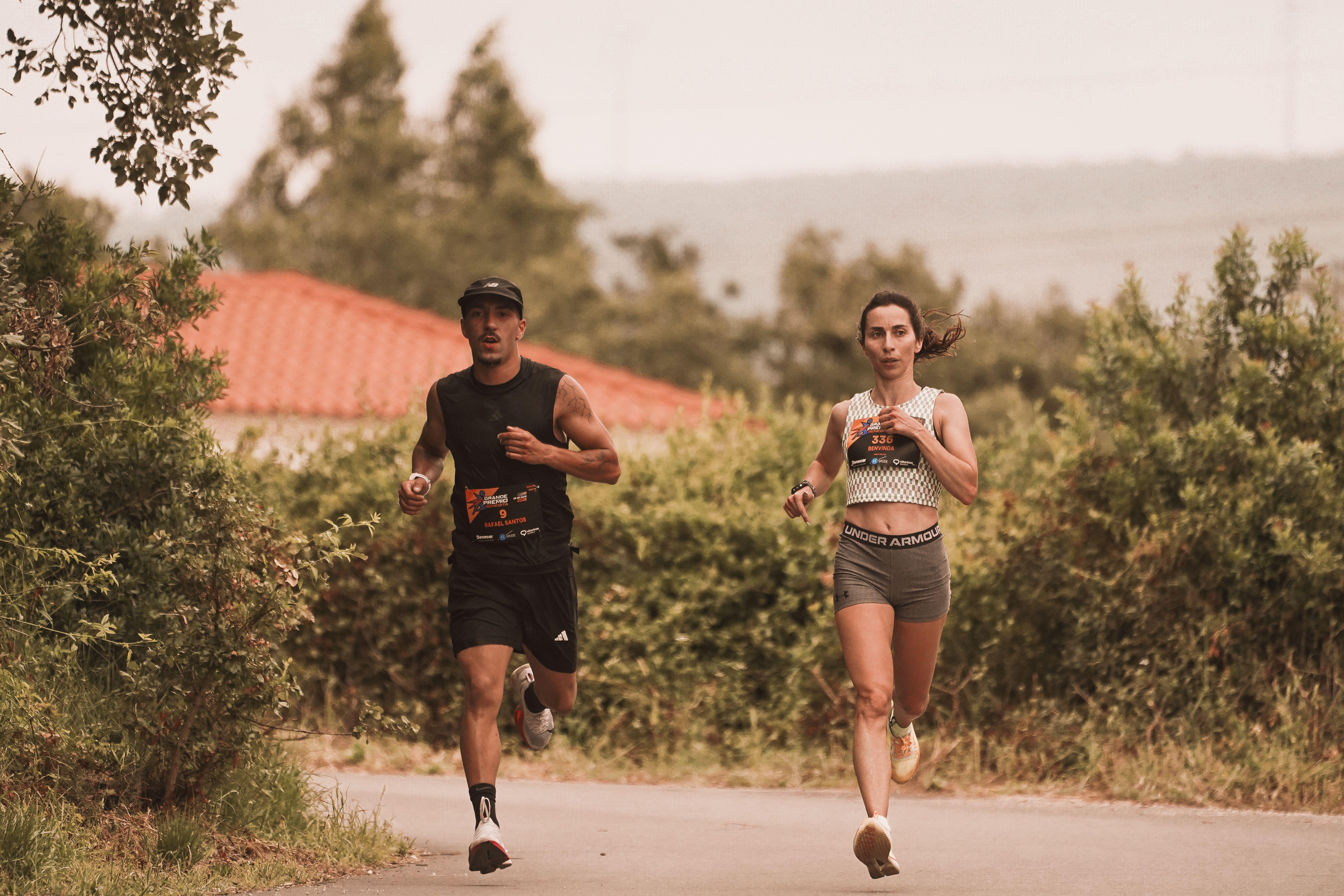 Two athletes jogging on an outdoor trail during a marathon, surrounded by greenery.