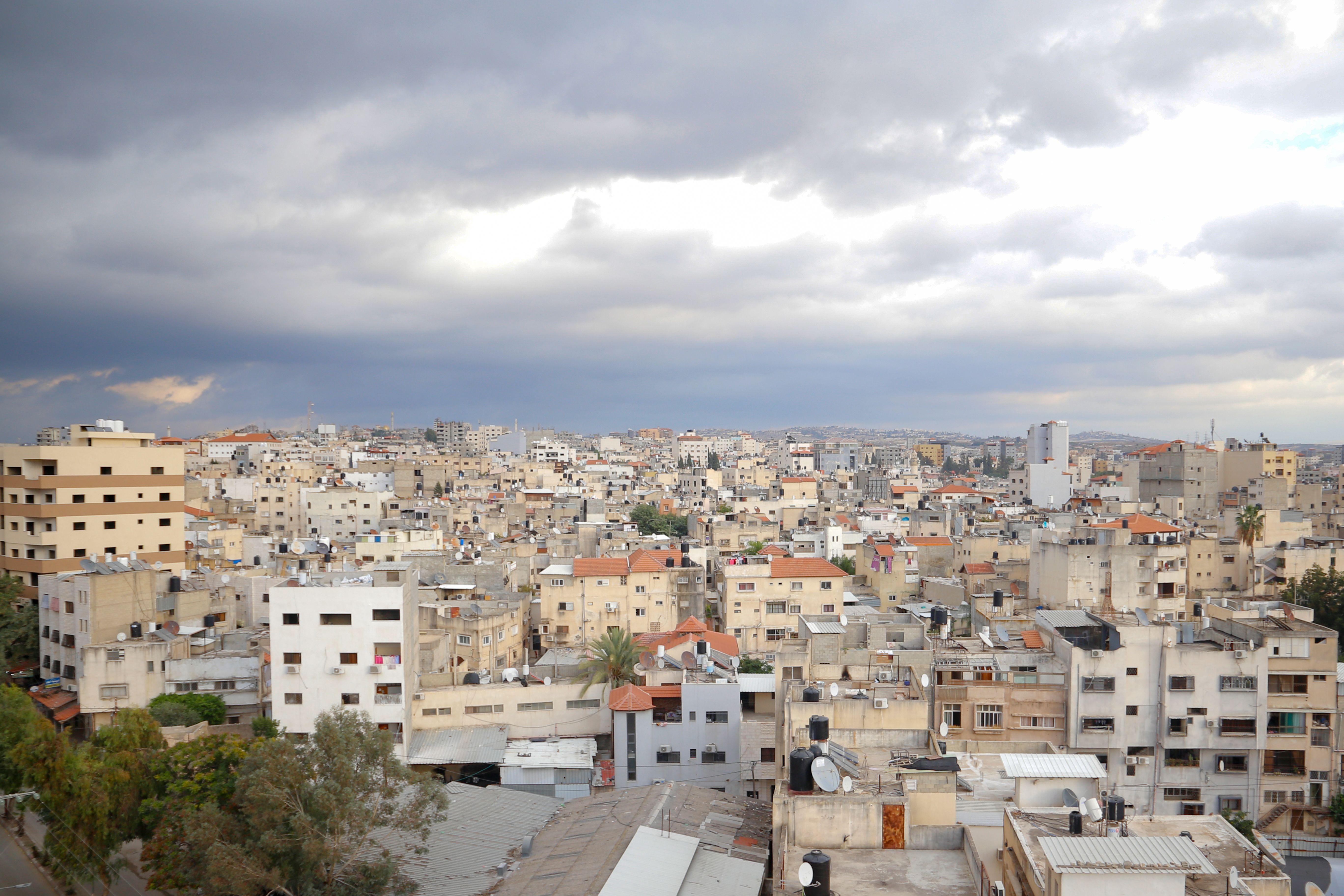 Aerial view of Qalqilya's urban cityscape under dramatic clouds, showcasing diverse architecture.