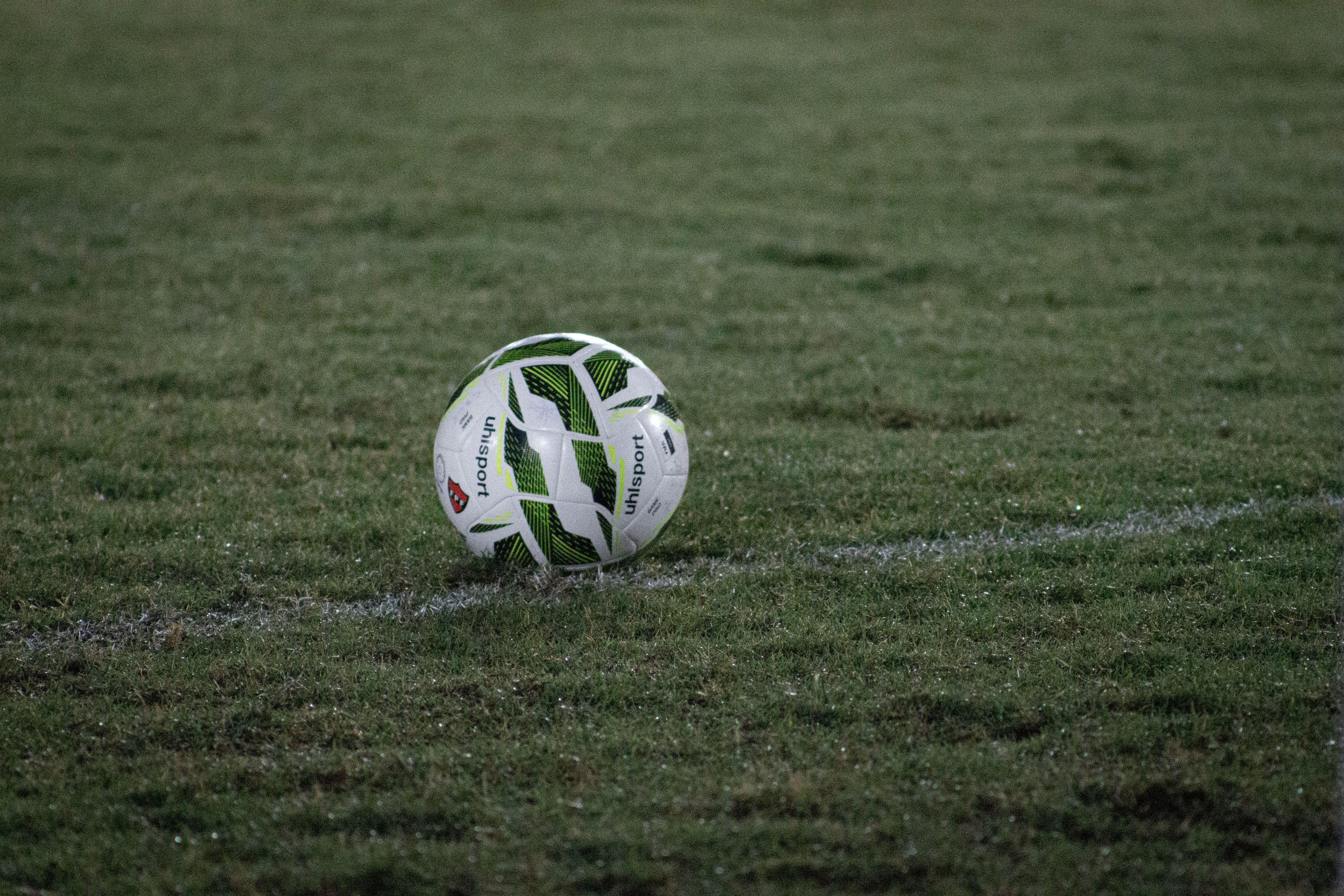 A soccer ball resting on a grass field, captured during nightfall with visible dew.