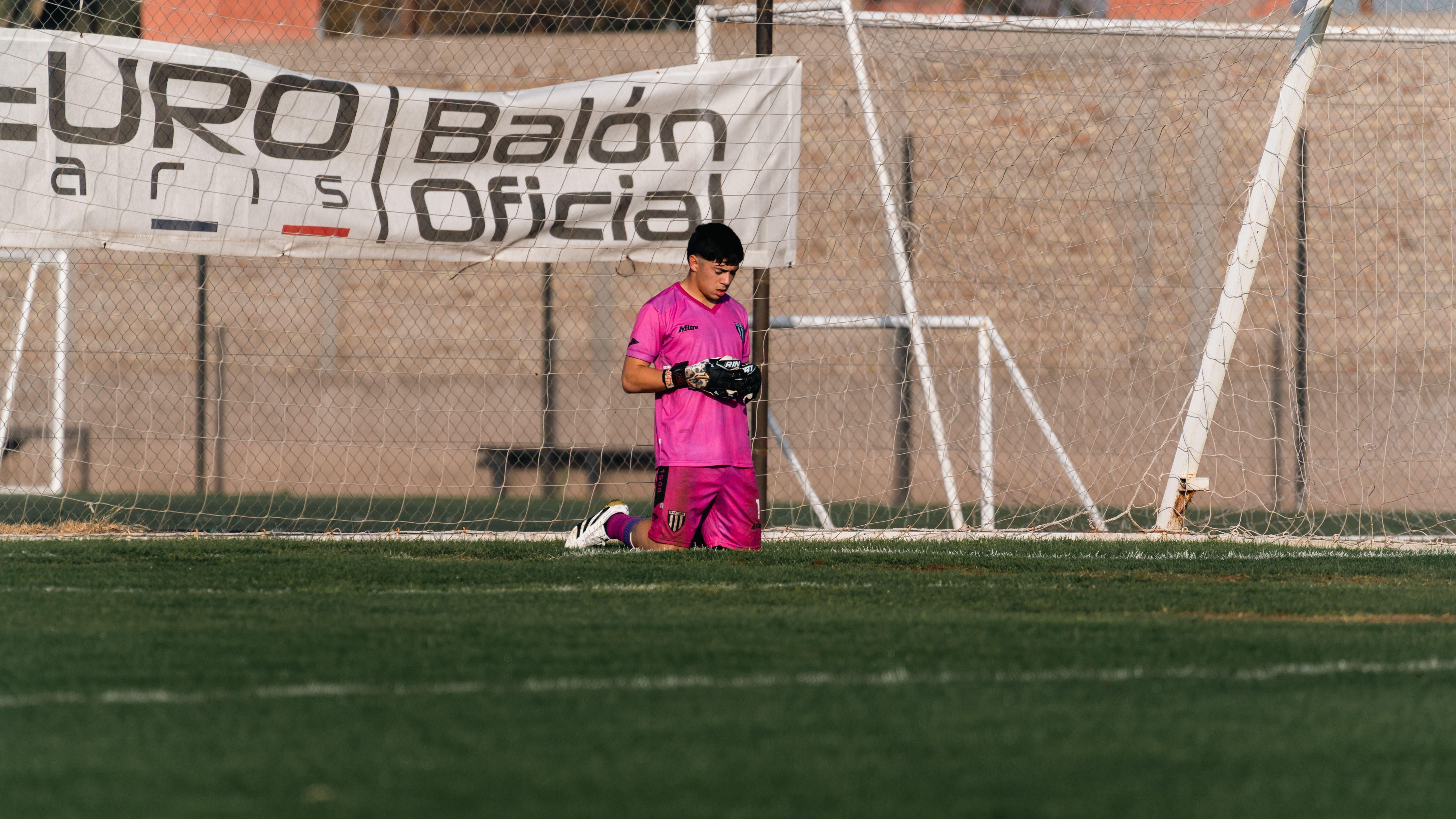 Young soccer goalkeeper in pink gear kneeling on the field during practice.