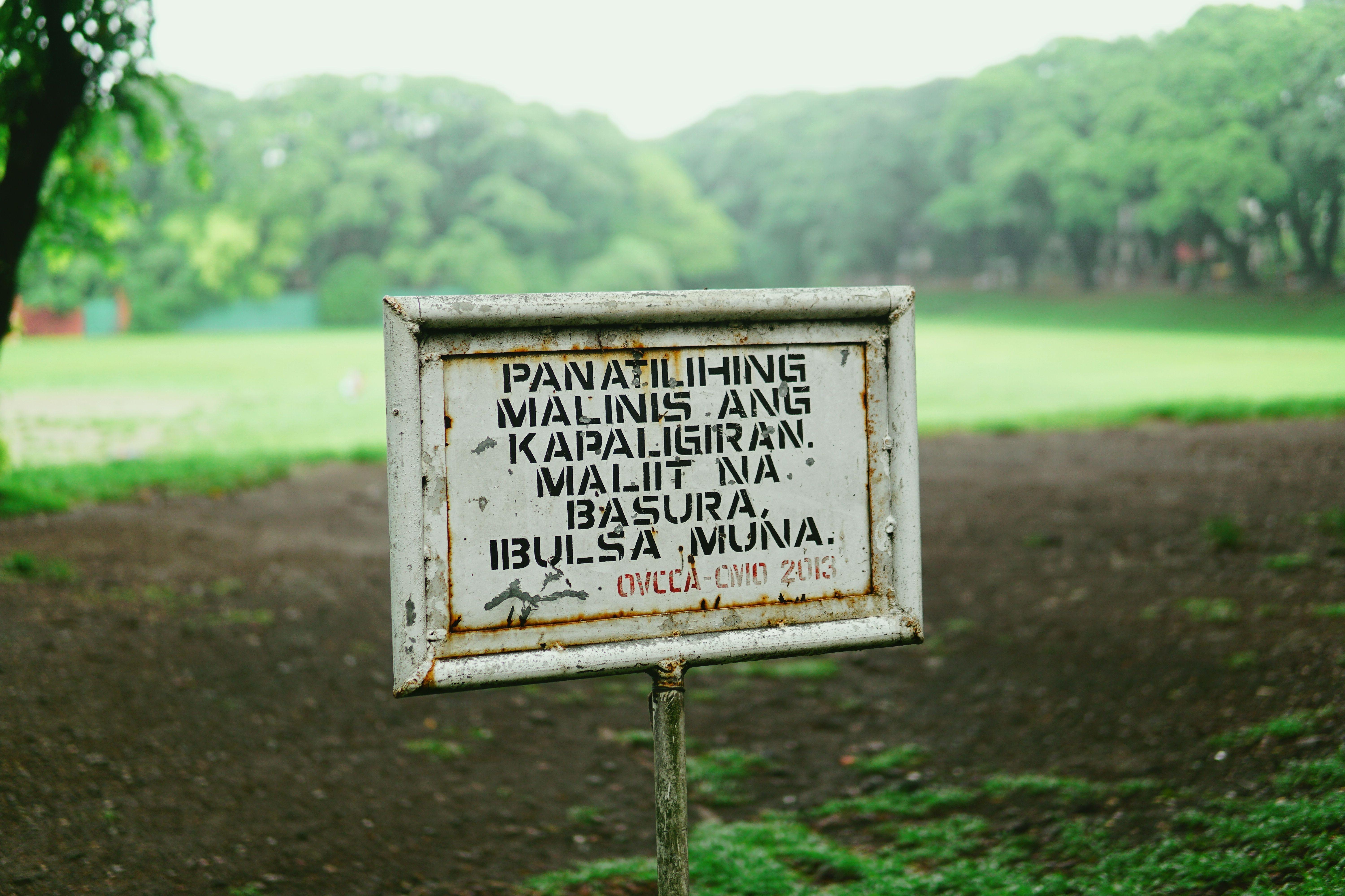 A weathered sign promotes cleanliness in a verdant park environment, emphasizing conservation.