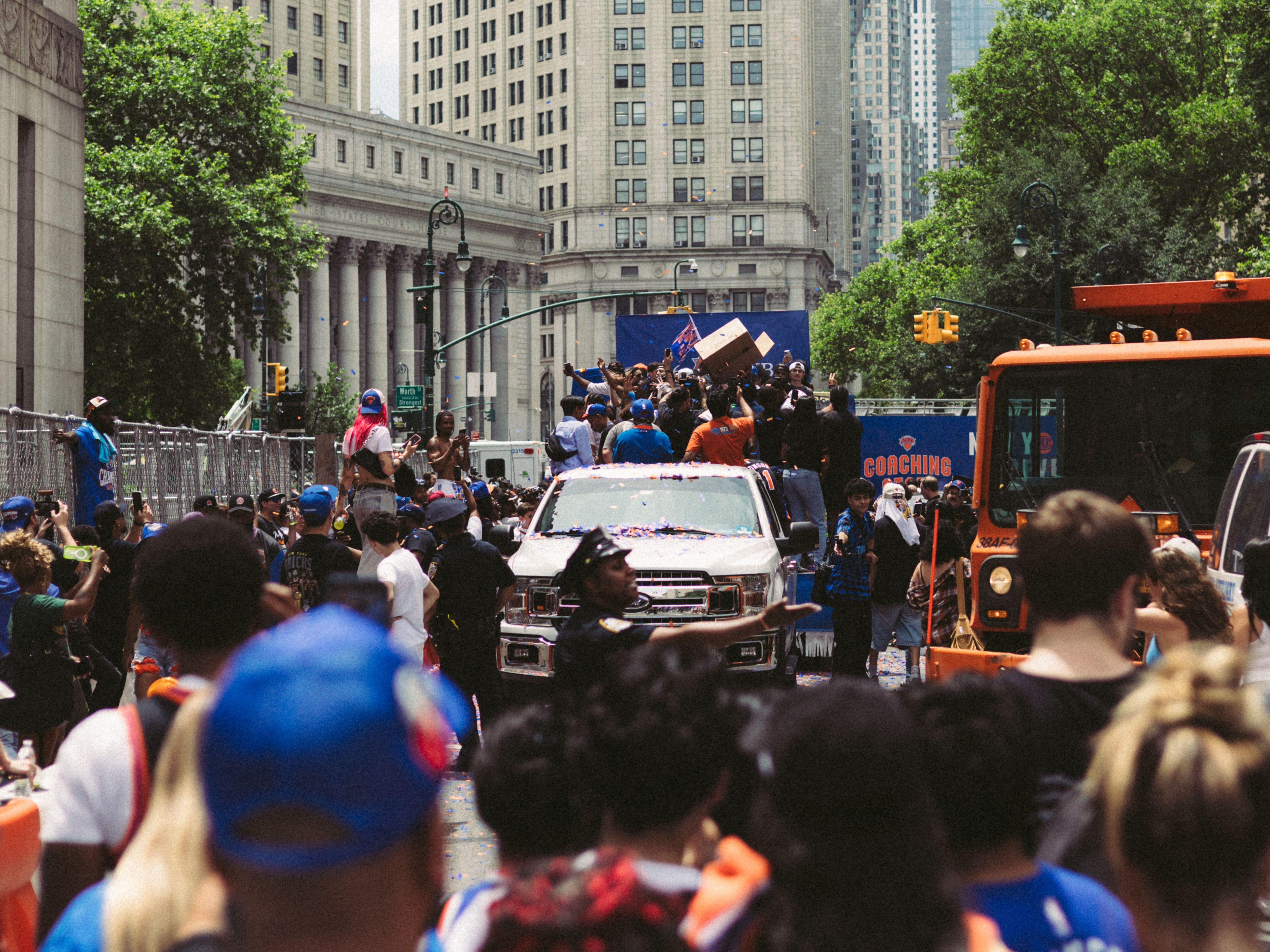 Energetic city parade with cheering crowd and vehicles in urban environment.