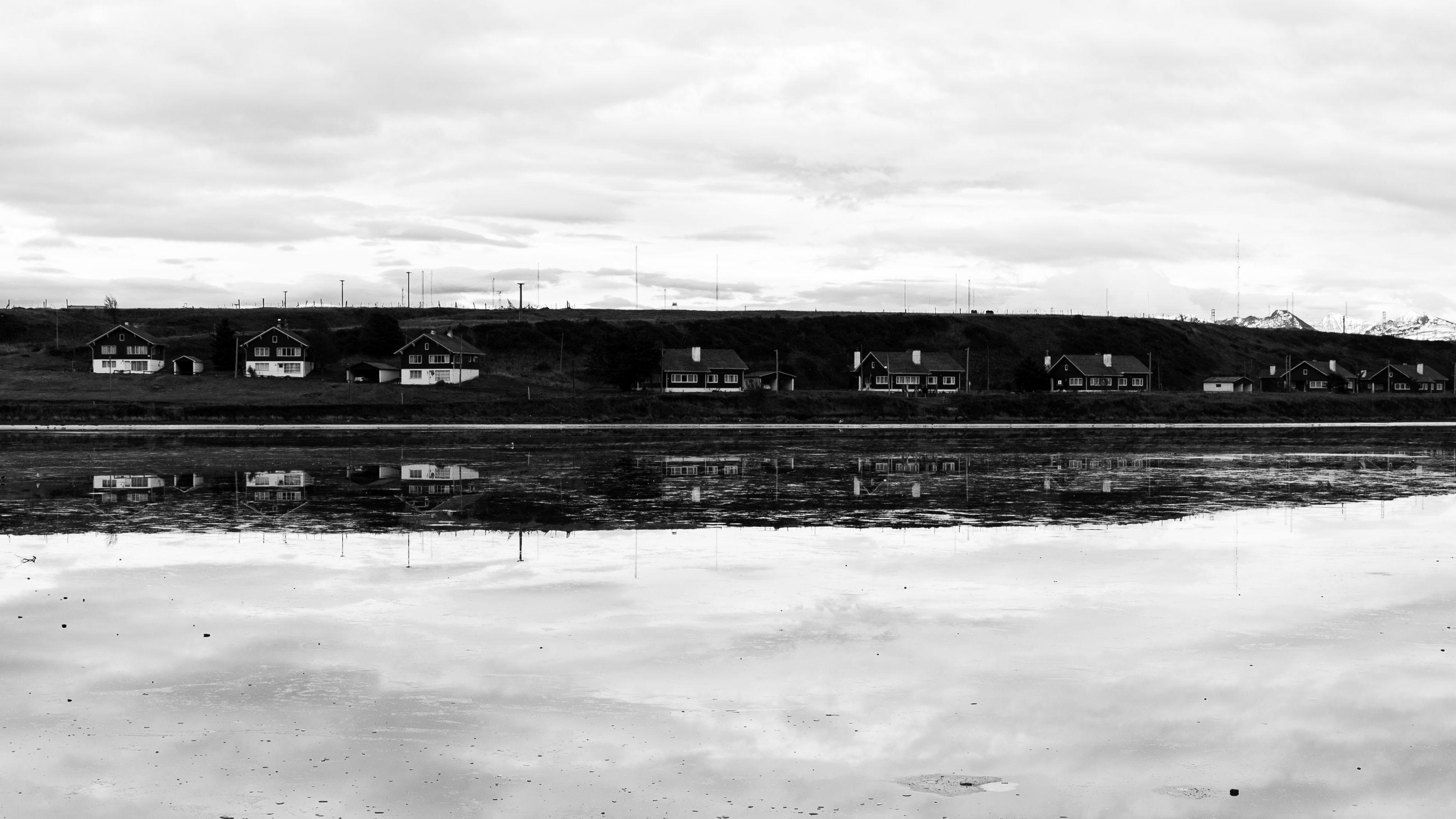 Monochrome view of Ushuaia houses reflected in still water, showcasing tranquil Argentine scenery.