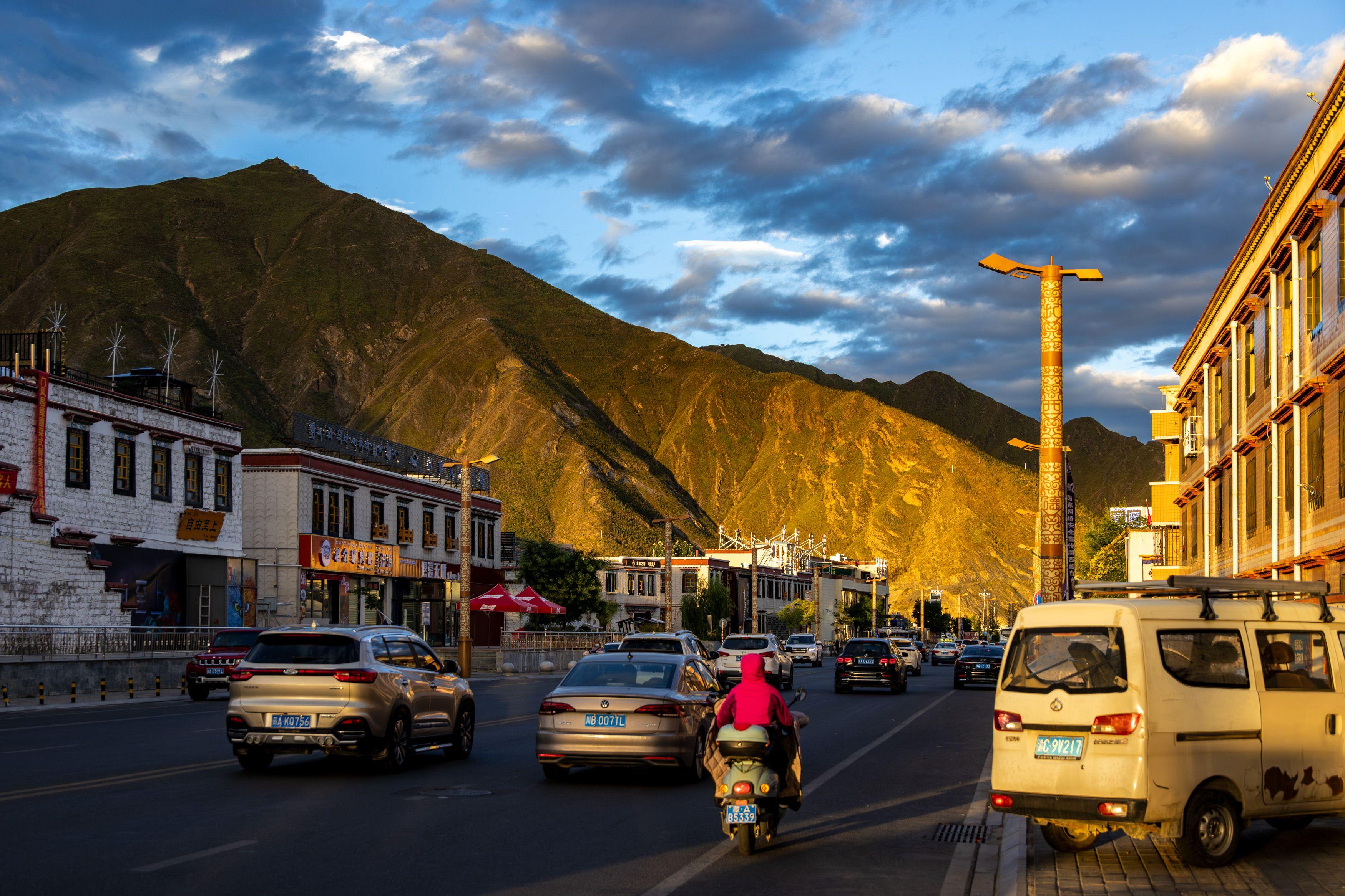 Busy street in a Tibetan town near mountains at sunset, capturing golden hour light.