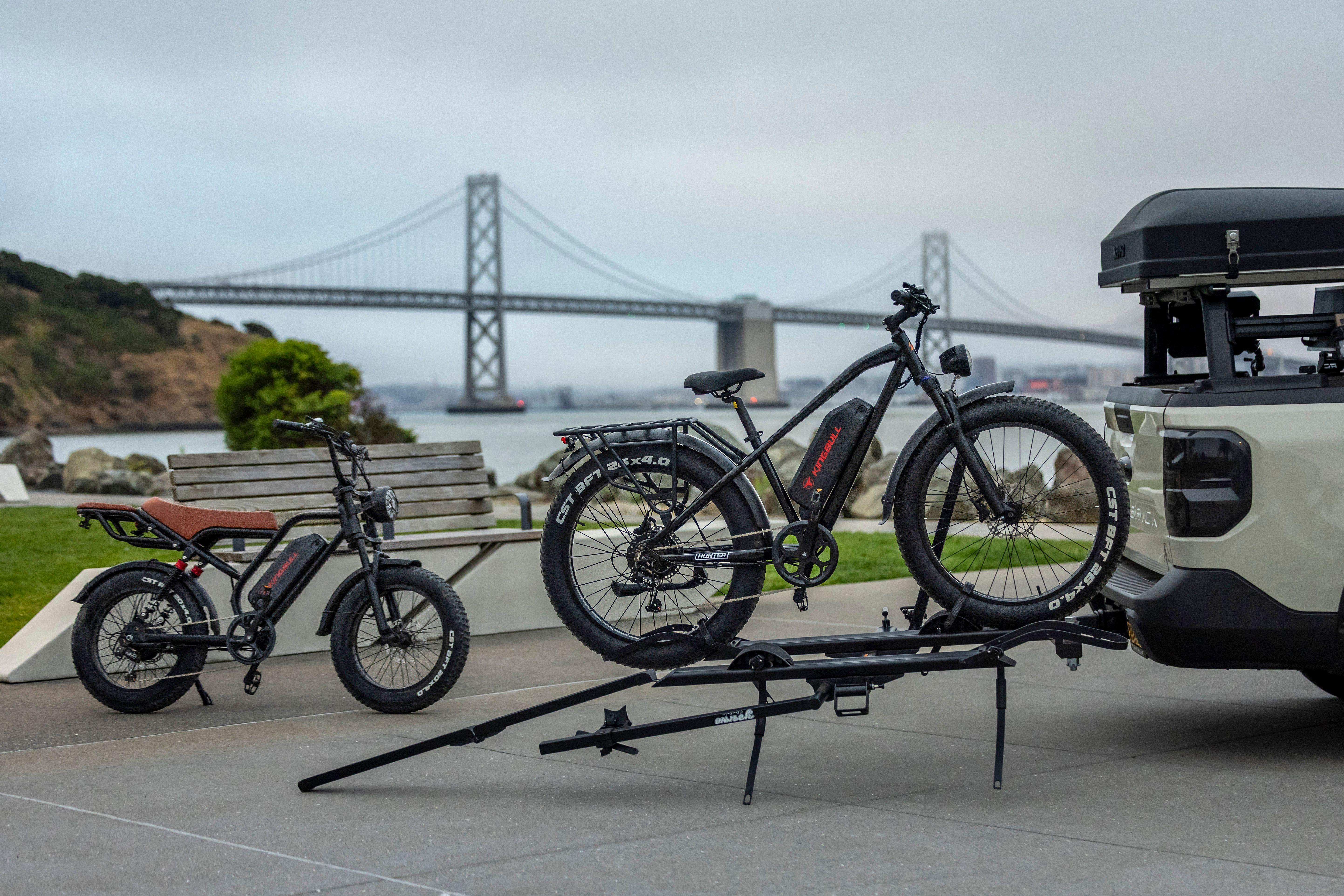 Electric bicycles parked near the iconic San Francisco Bay Bridge on a cloudy day.