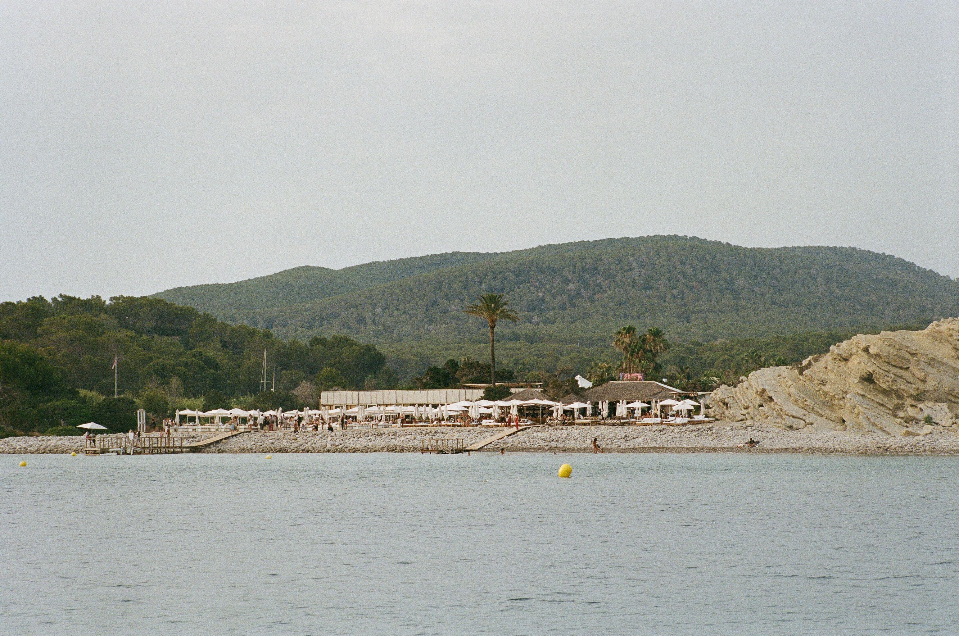 Serene beach scene in Eivissa with lush green hills and a distant resort.