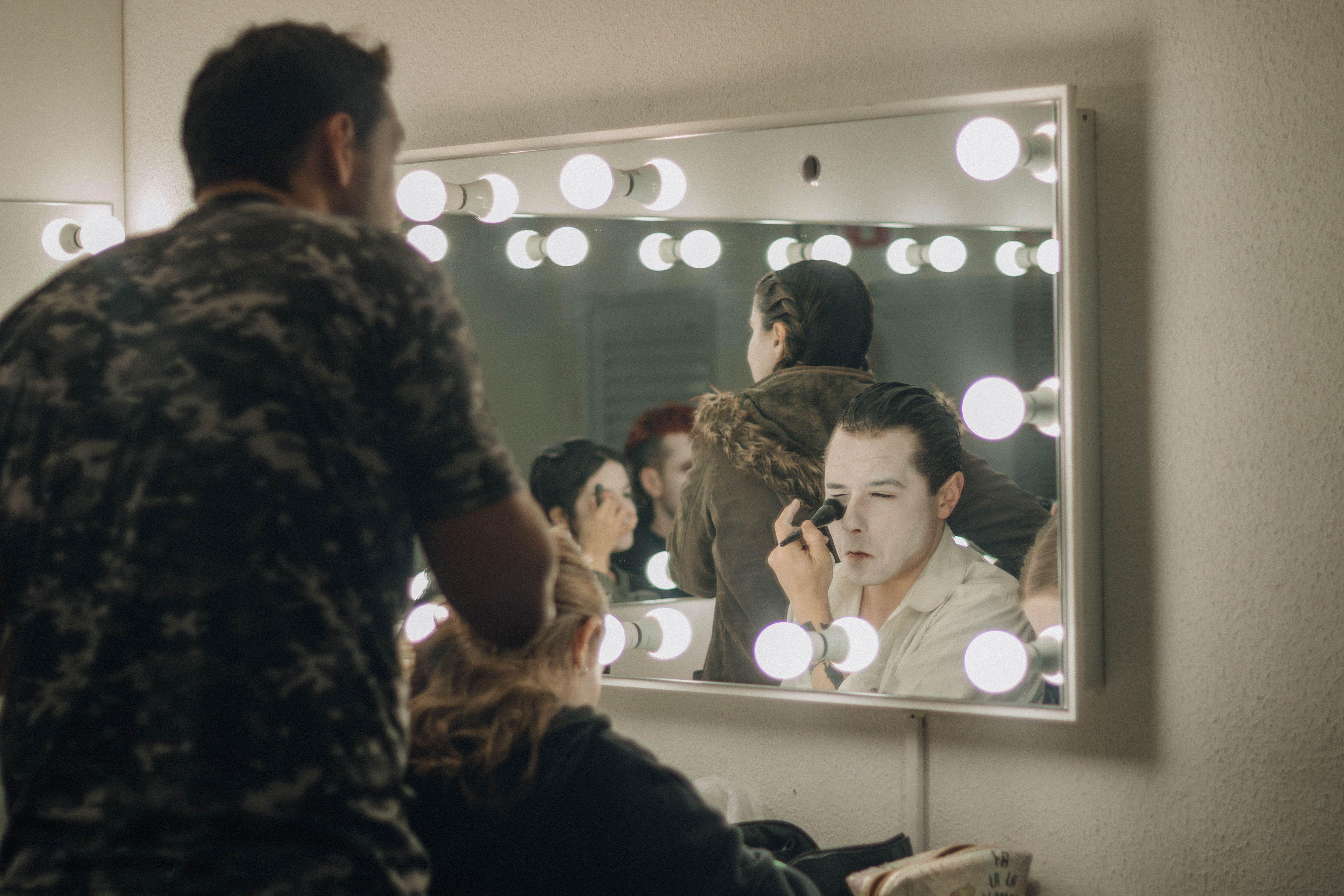 Actors applying makeup backstage in illuminated dressing room before a performance.