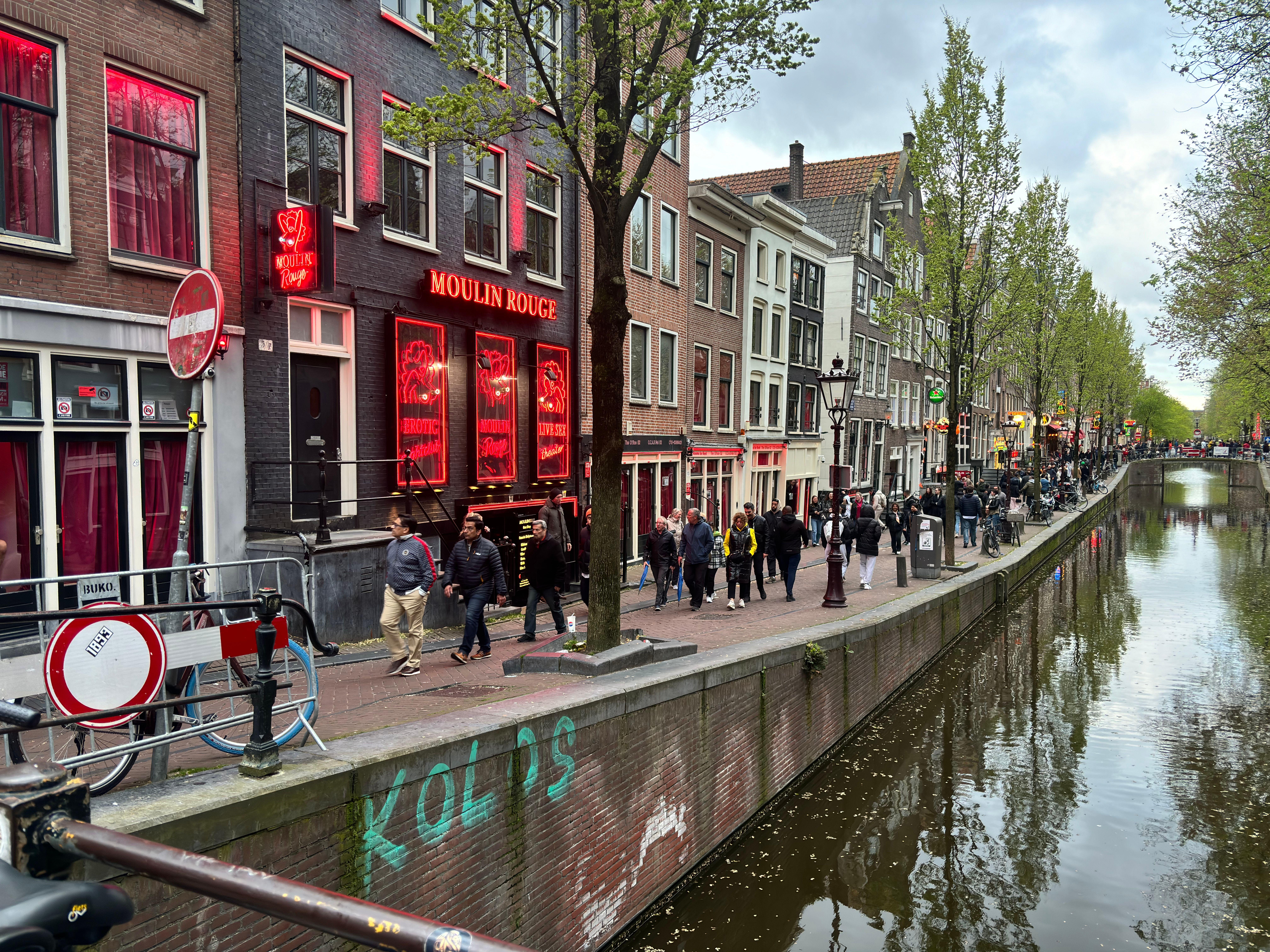 Bustling street scene in Amsterdam's Red Light District with iconic Moulin Rouge.