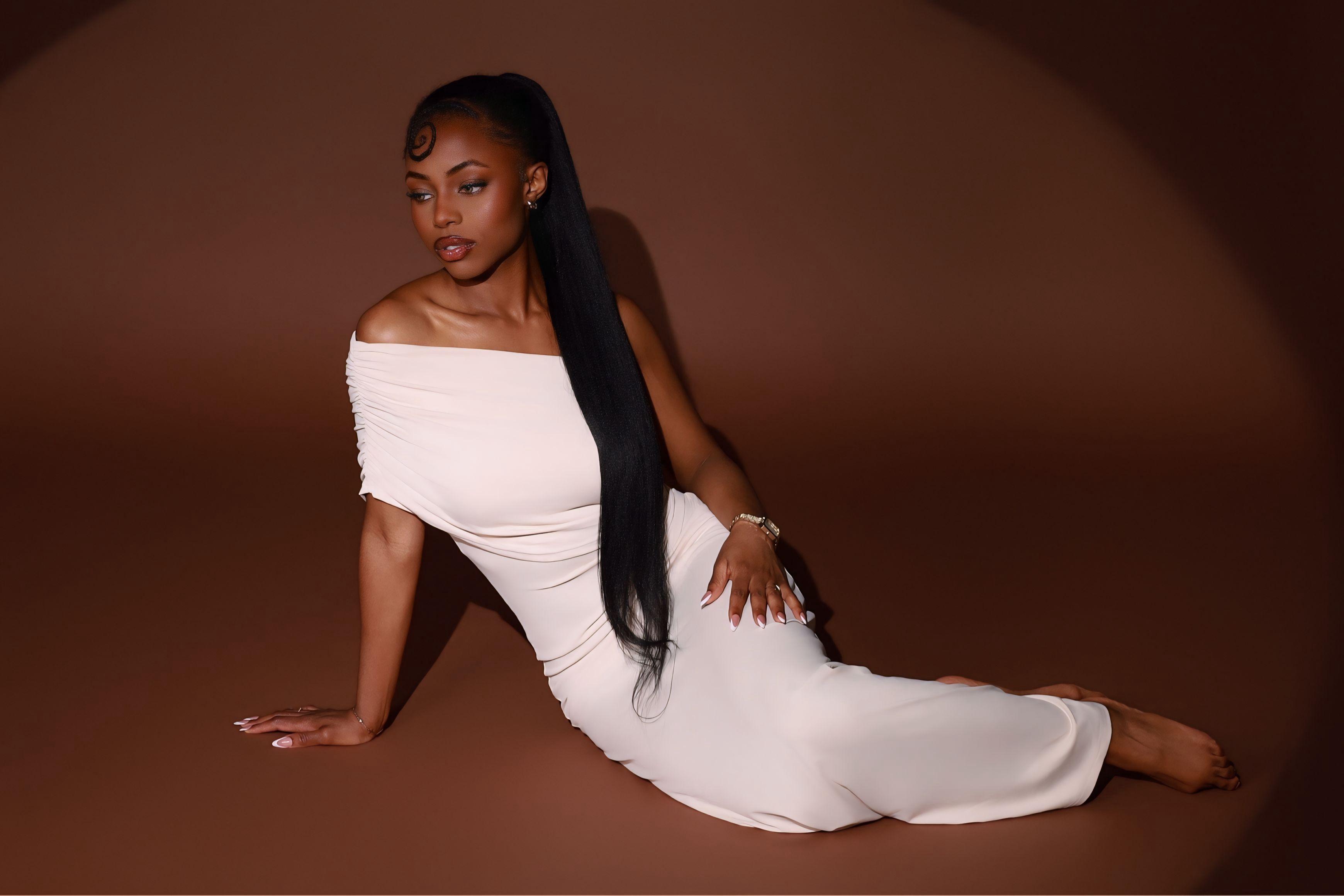 Elegant portrait of a Black woman in an off-shoulder white dress with a brown backdrop.