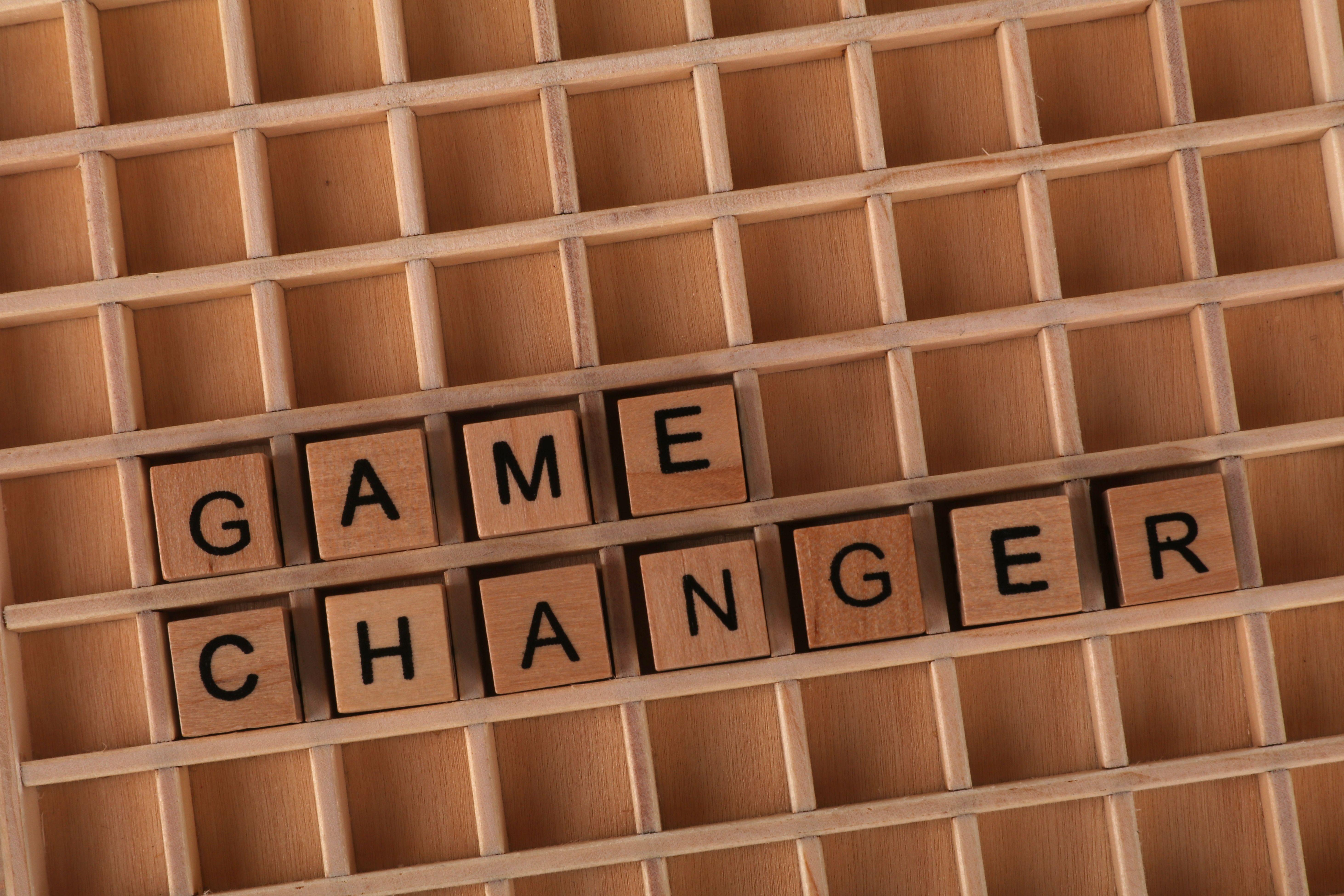 Scrabble tiles forming 'Game Changer' on a wooden grid, symbolizing innovation or transformation.