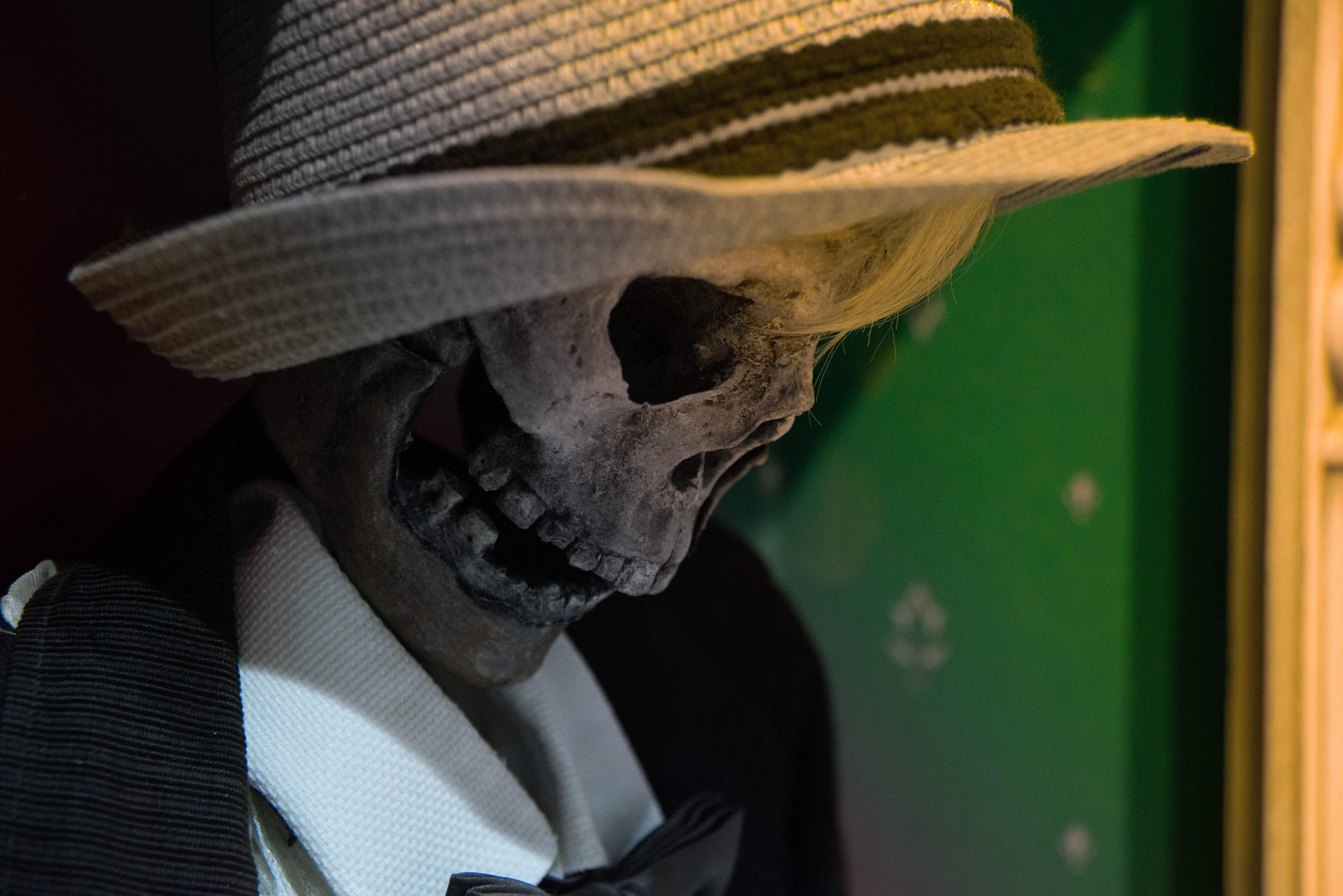 A skeleton adorned with a straw hat and formal suit in a dimly lit setting.