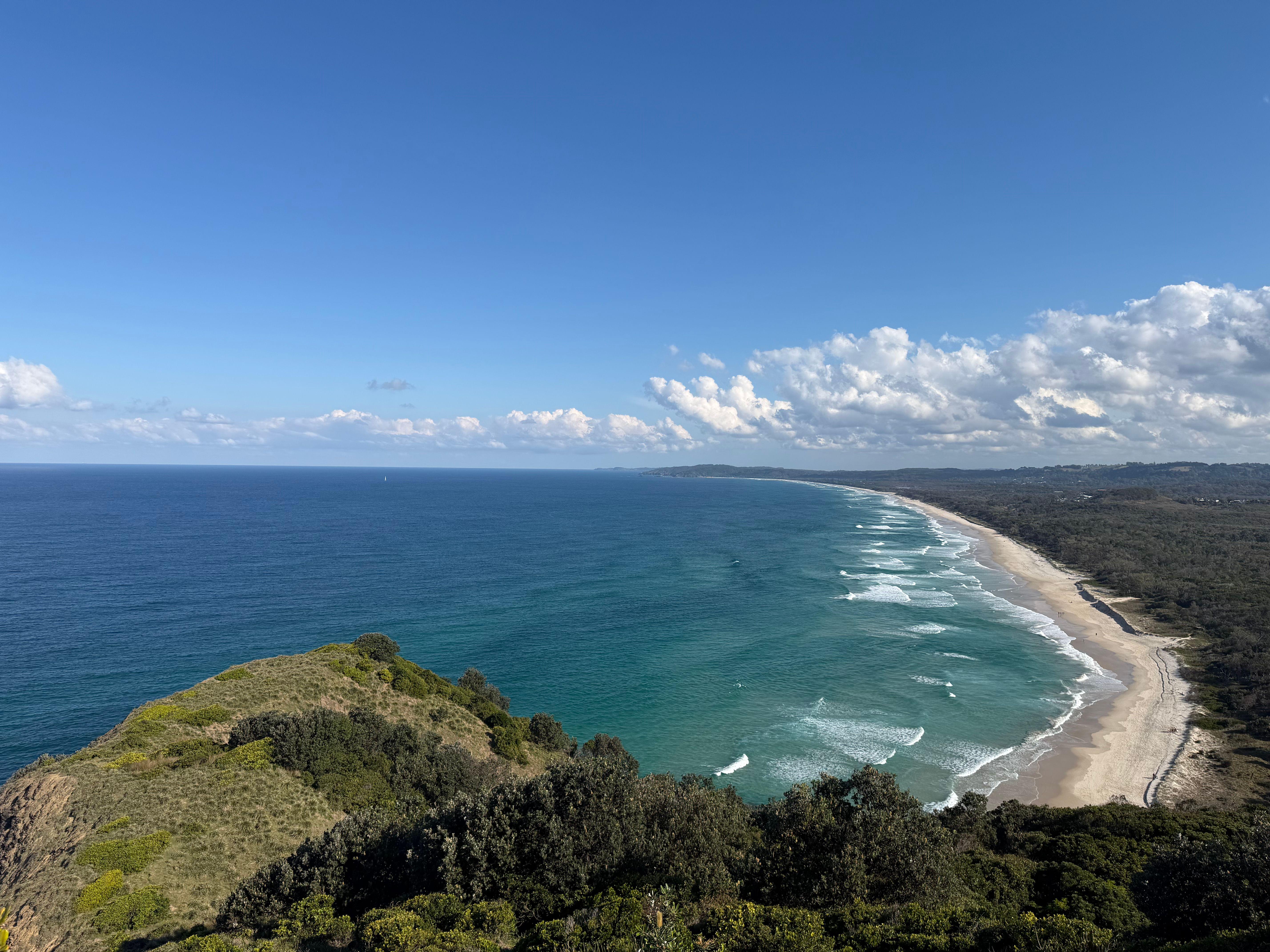 Stunning aerial photo of Byron Bay coastline with lush greenery and expansive ocean under a clear blue sky.