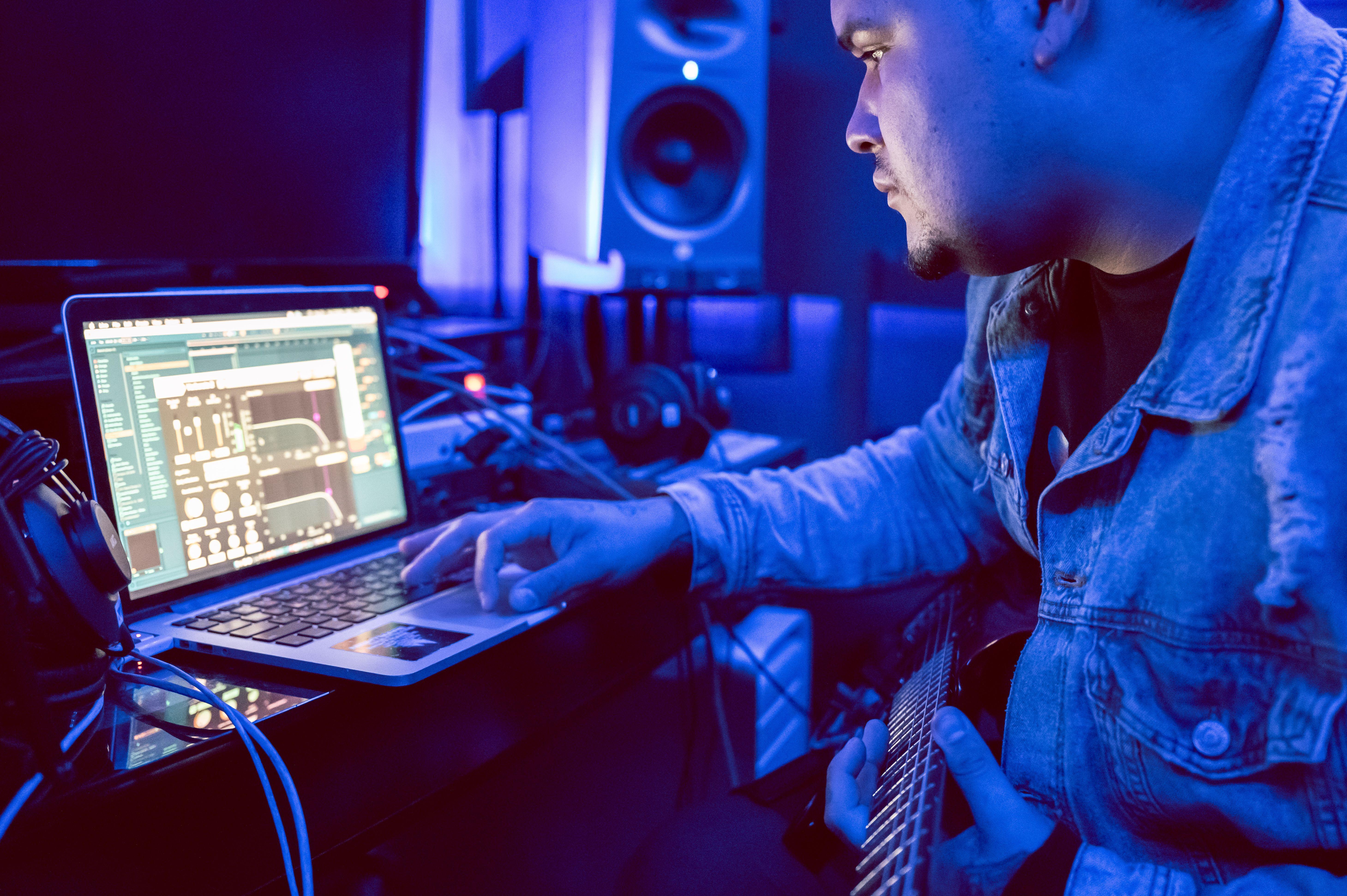 Young musician using laptop for music production in recording studio.