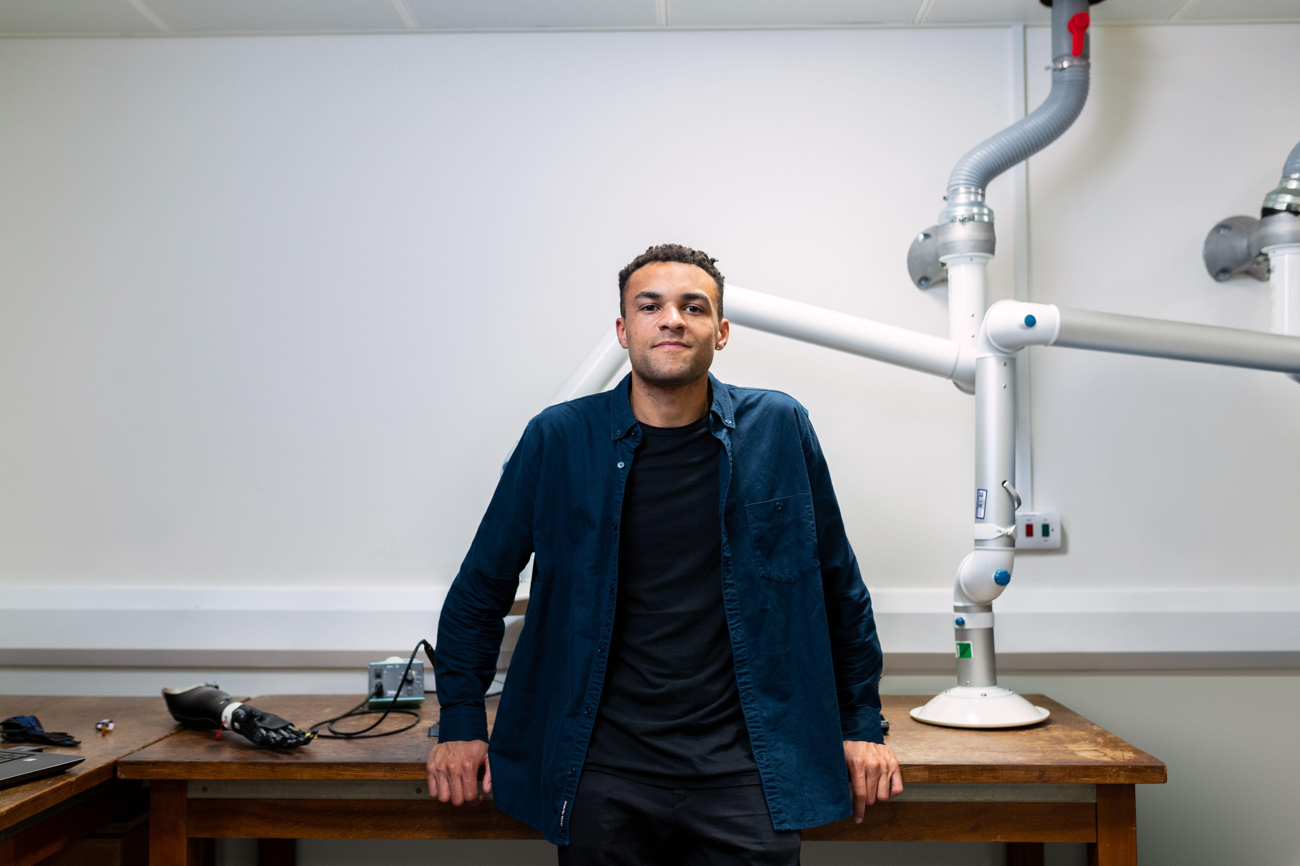 Confident young engineer standing in a laboratory with advanced robotic equipment.