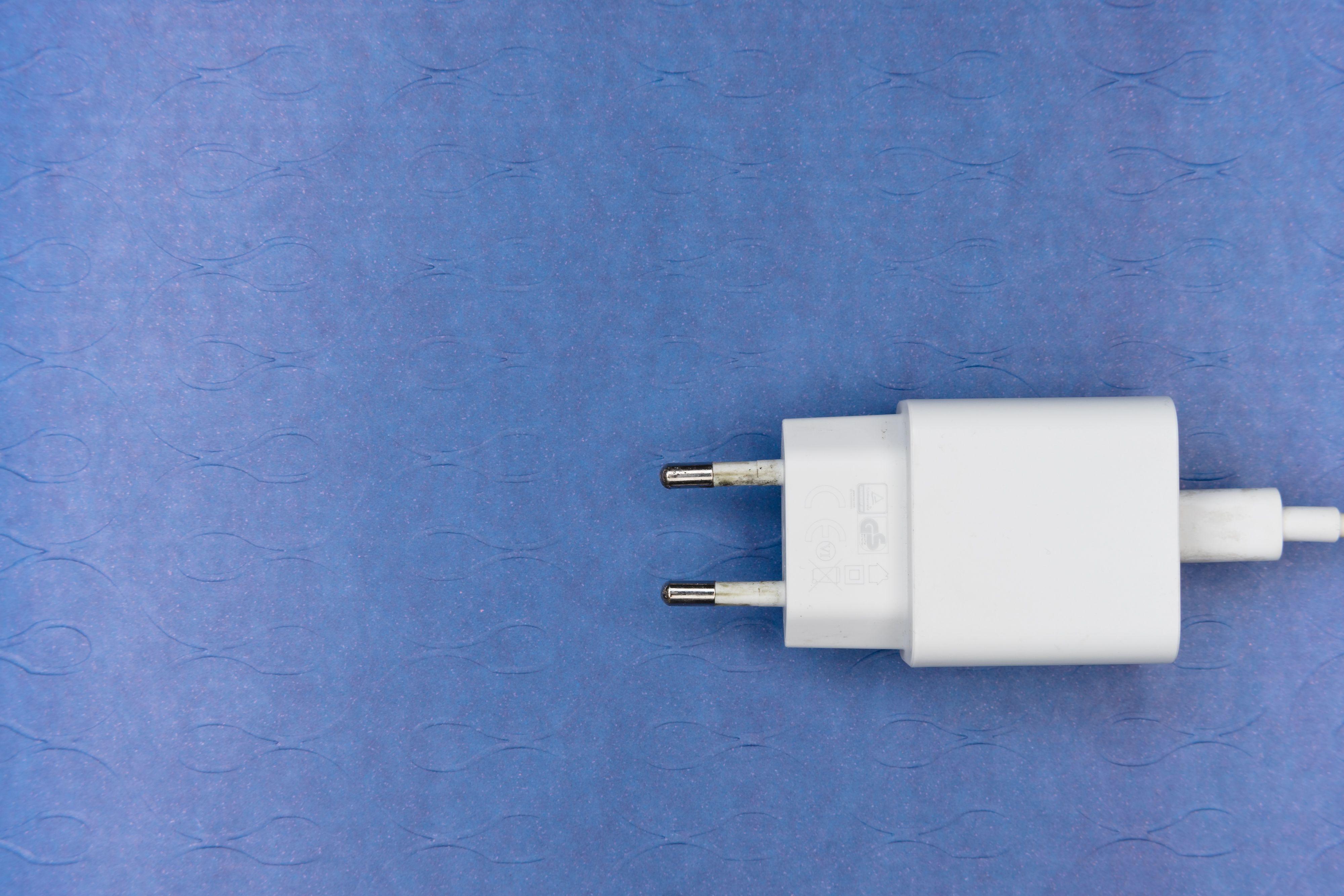 Close-up of a white electrical charger plug on a blue textured background, ideal for tech themes.