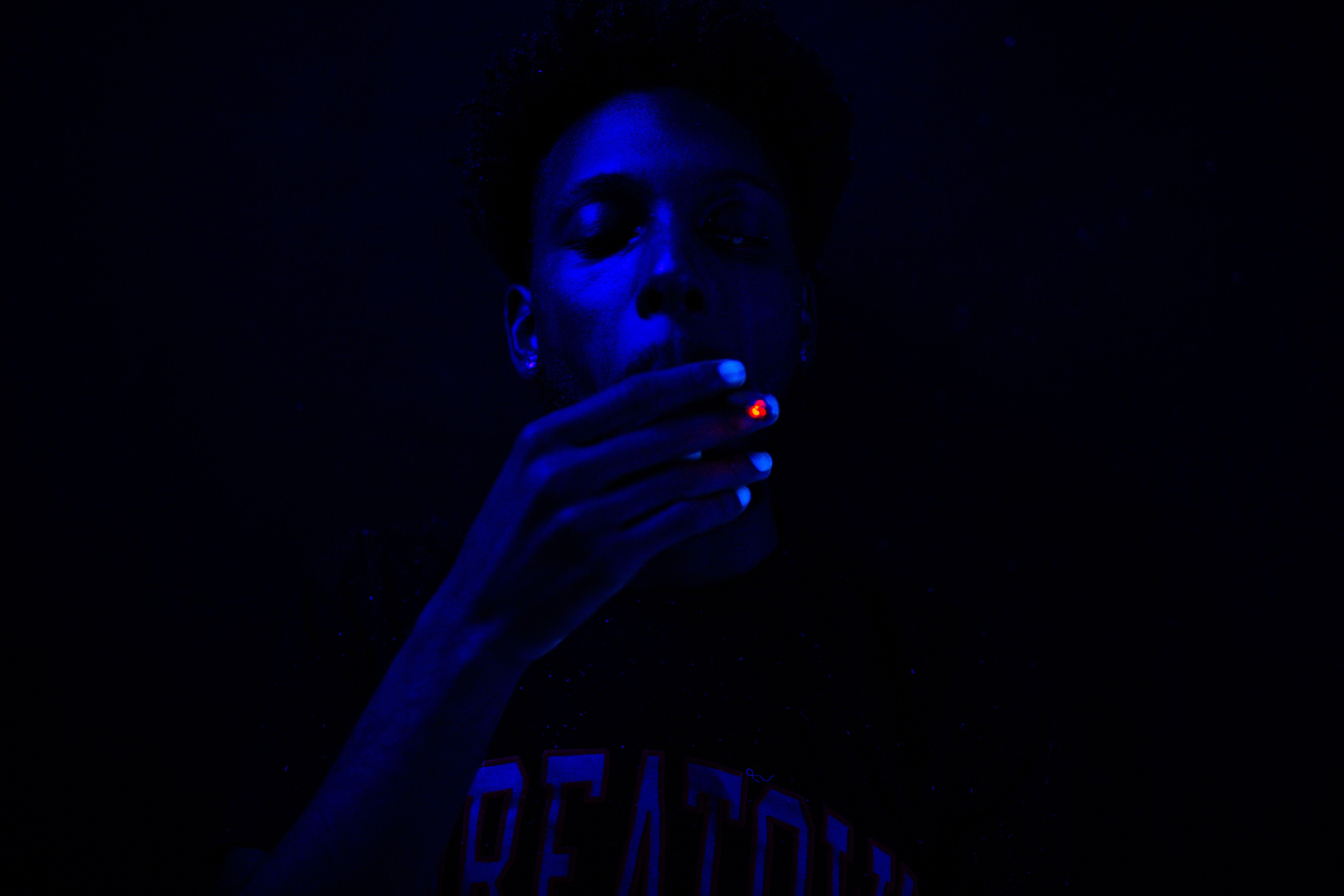 Close-up of a man smoking under blue ultraviolet lighting, creating a dramatic effect.