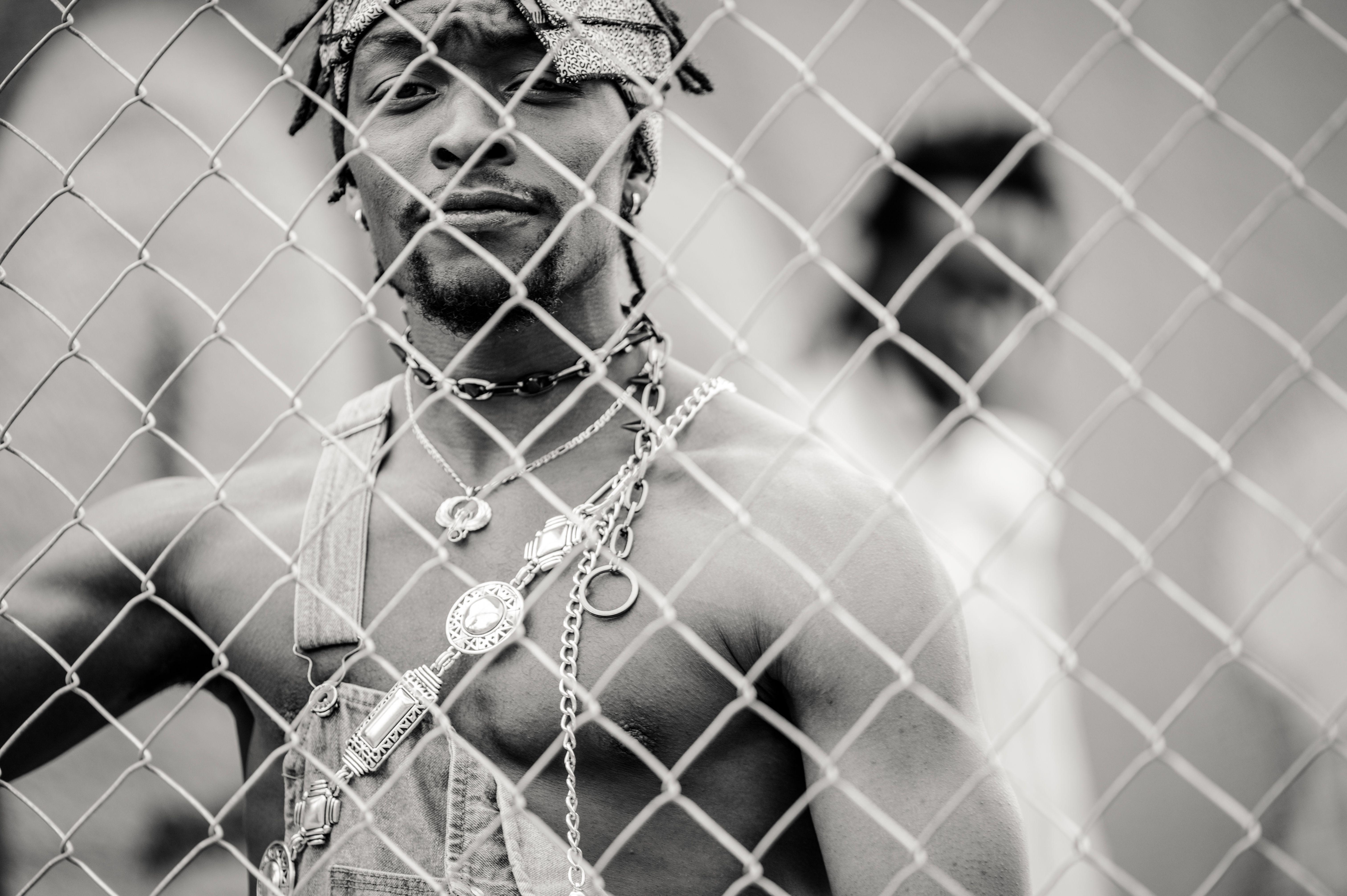 Black and white handsome sporty African American man with beard looking at camera through metallic chain link fence