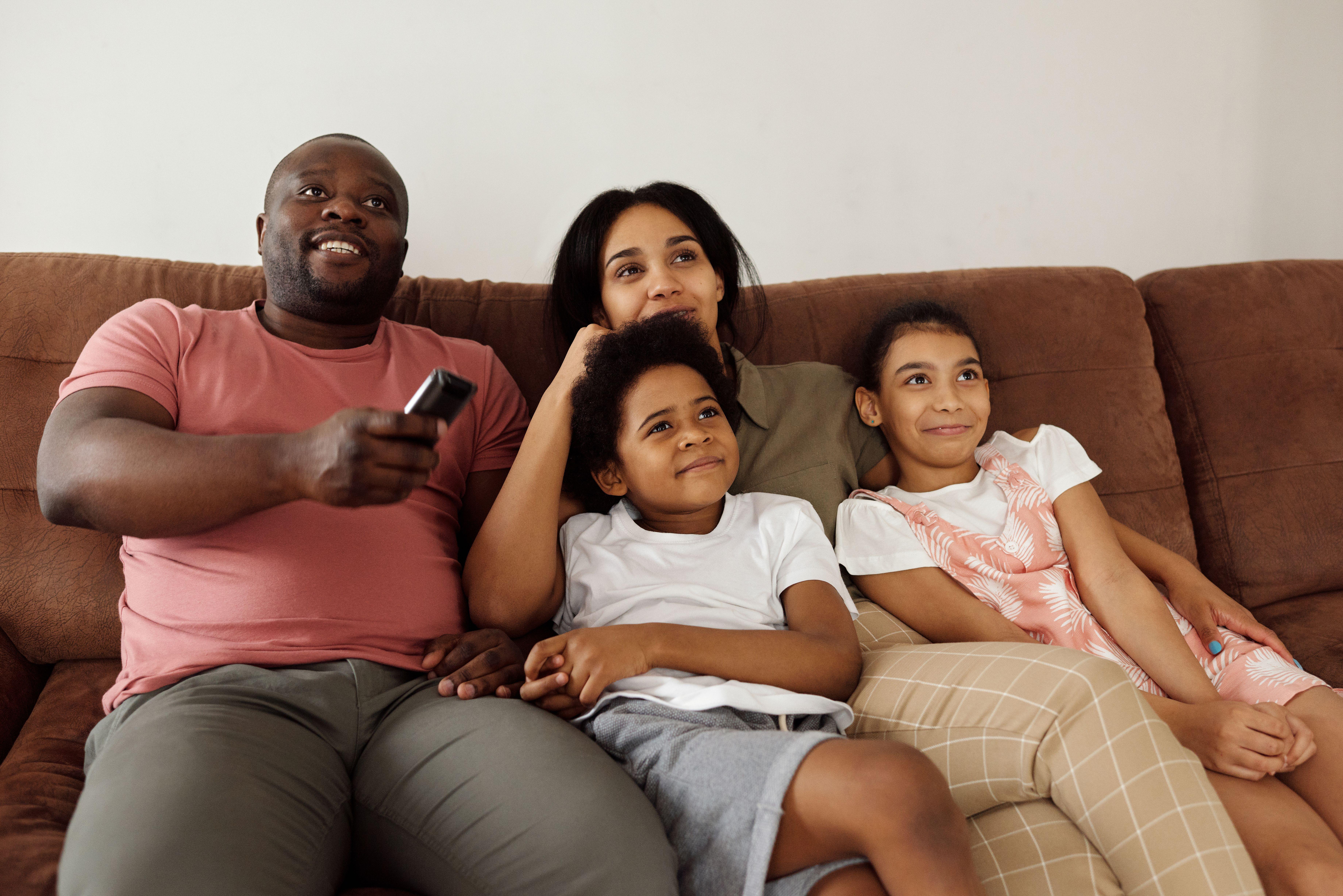 A family of four enjoying quality time together on the sofa, watching TV with smiling faces.