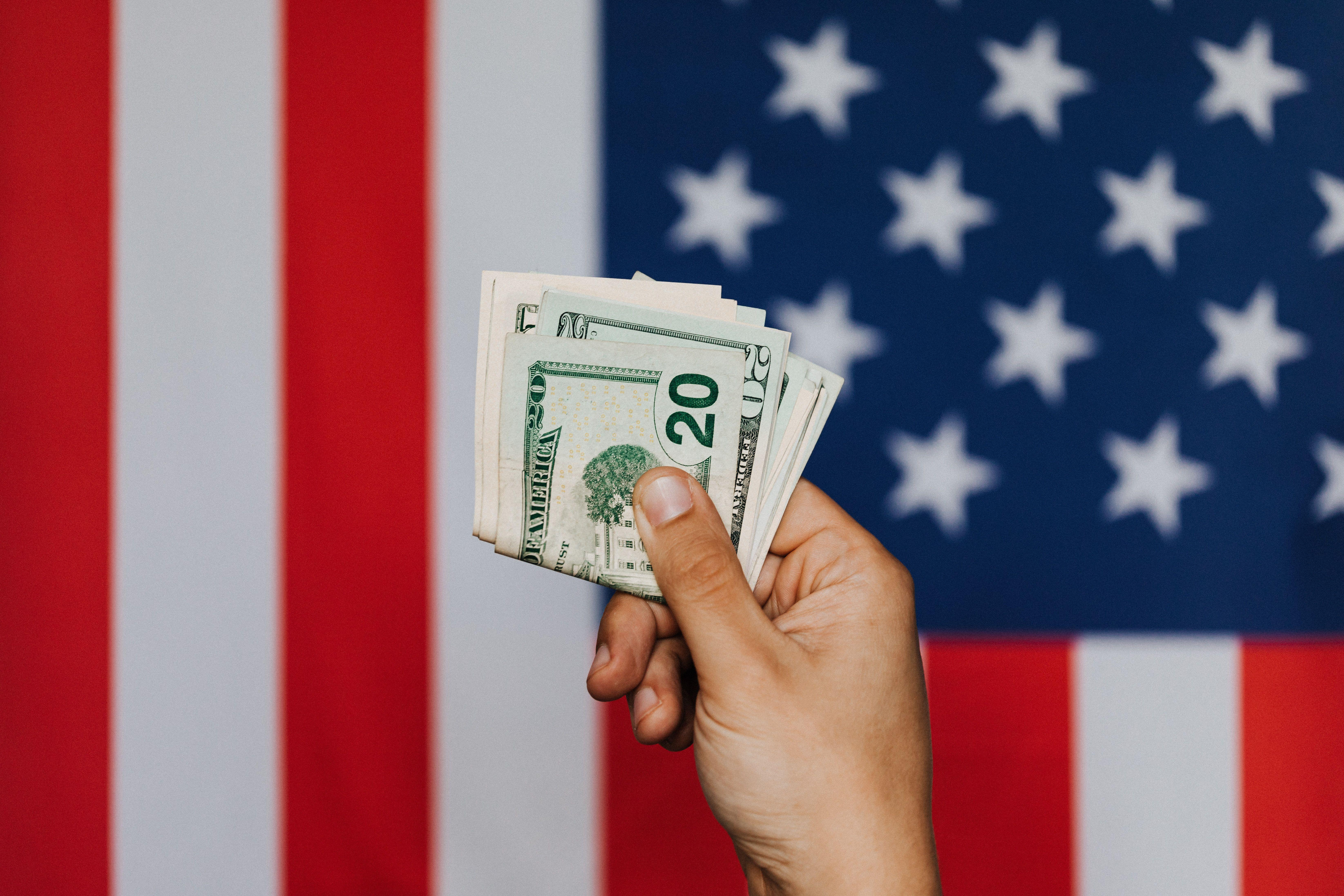 Unrecognizable male demonstrating dollars before official flag of USA on background