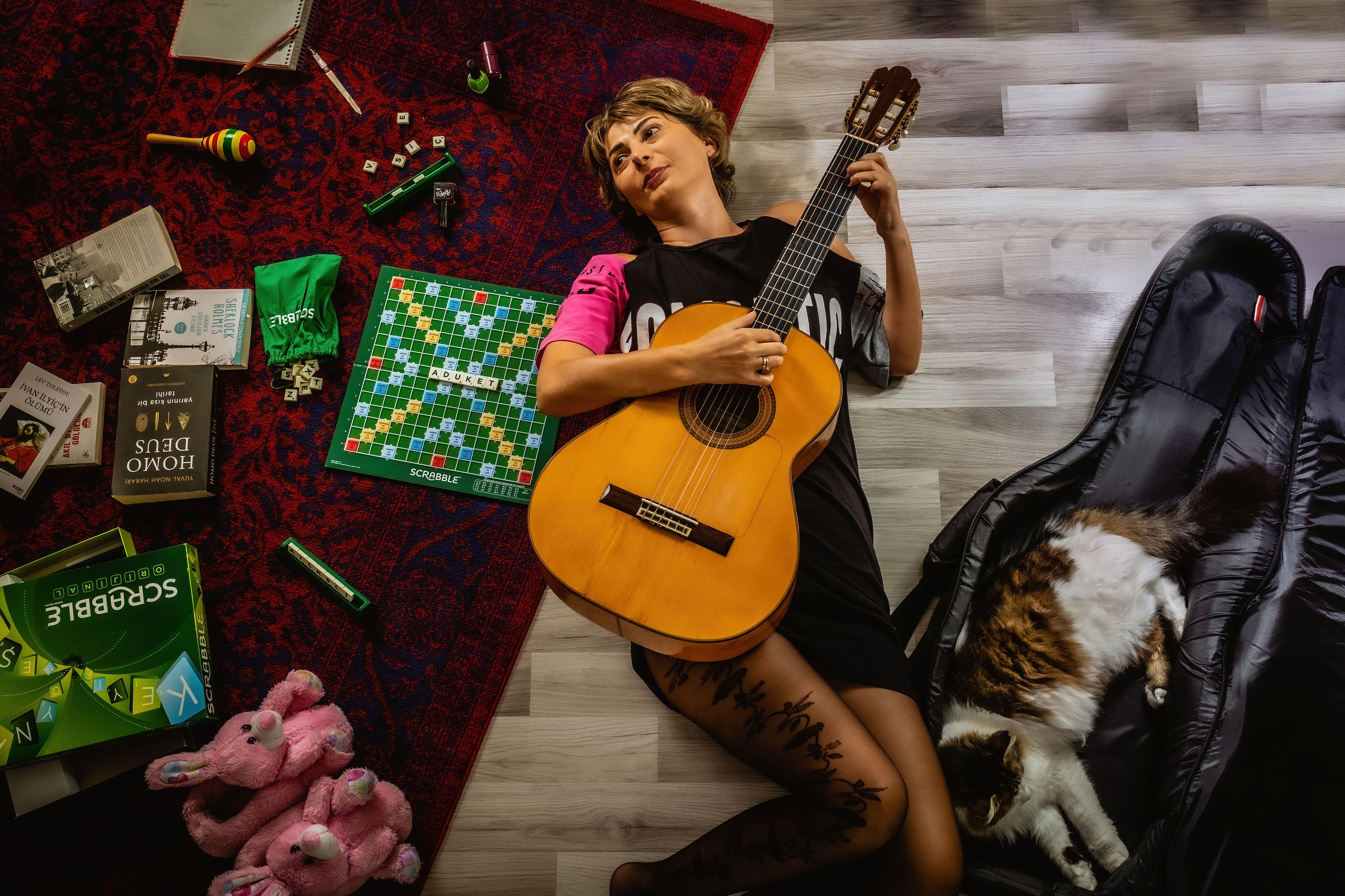 Woman playing guitar surrounded by board games and a sleeping cat, creating a cozy atmosphere.