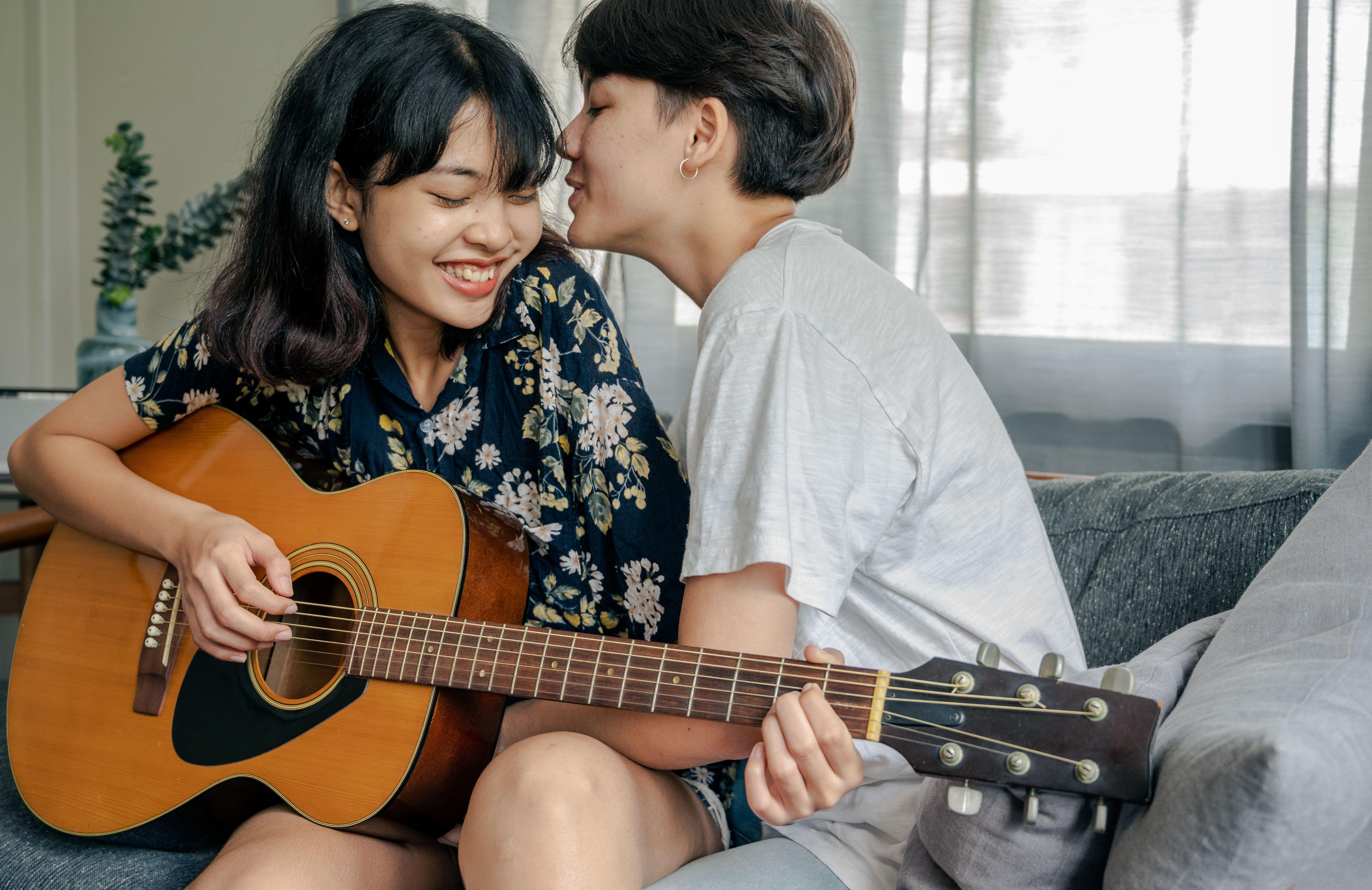 A joyful couple playing guitar and sharing affectionate moments indoors.